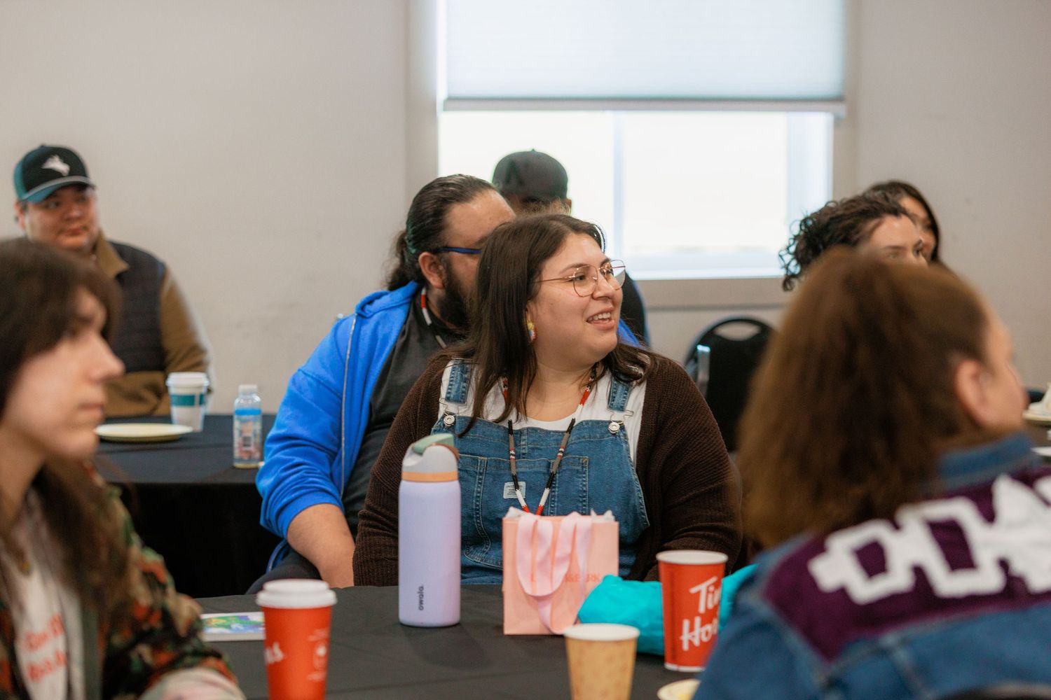People smiling and engaging at a community gathering around tables with colorful cups and drink bottles in a bright room.