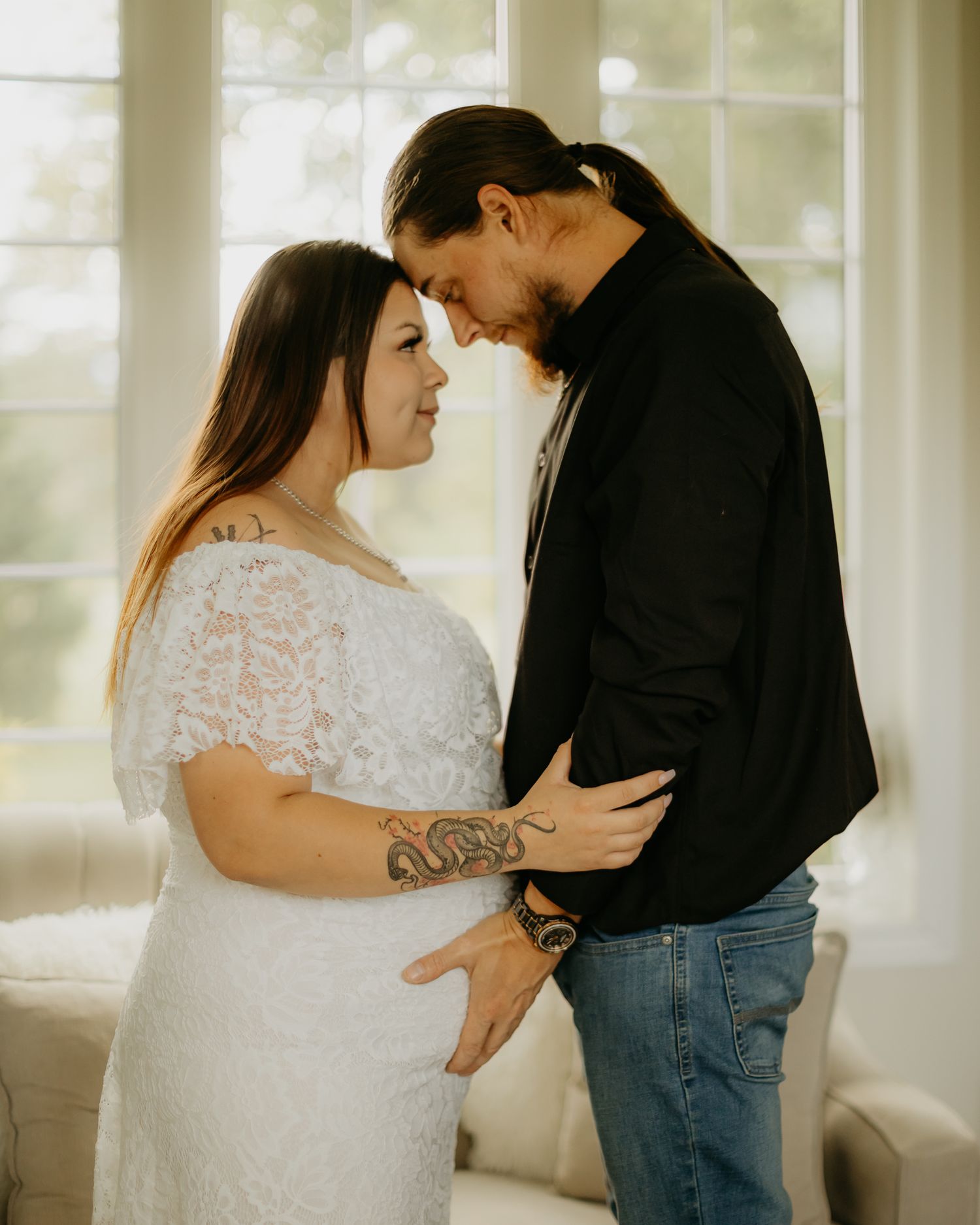 Couple embracing in sunlit room wearing white lace and black casual outfits.