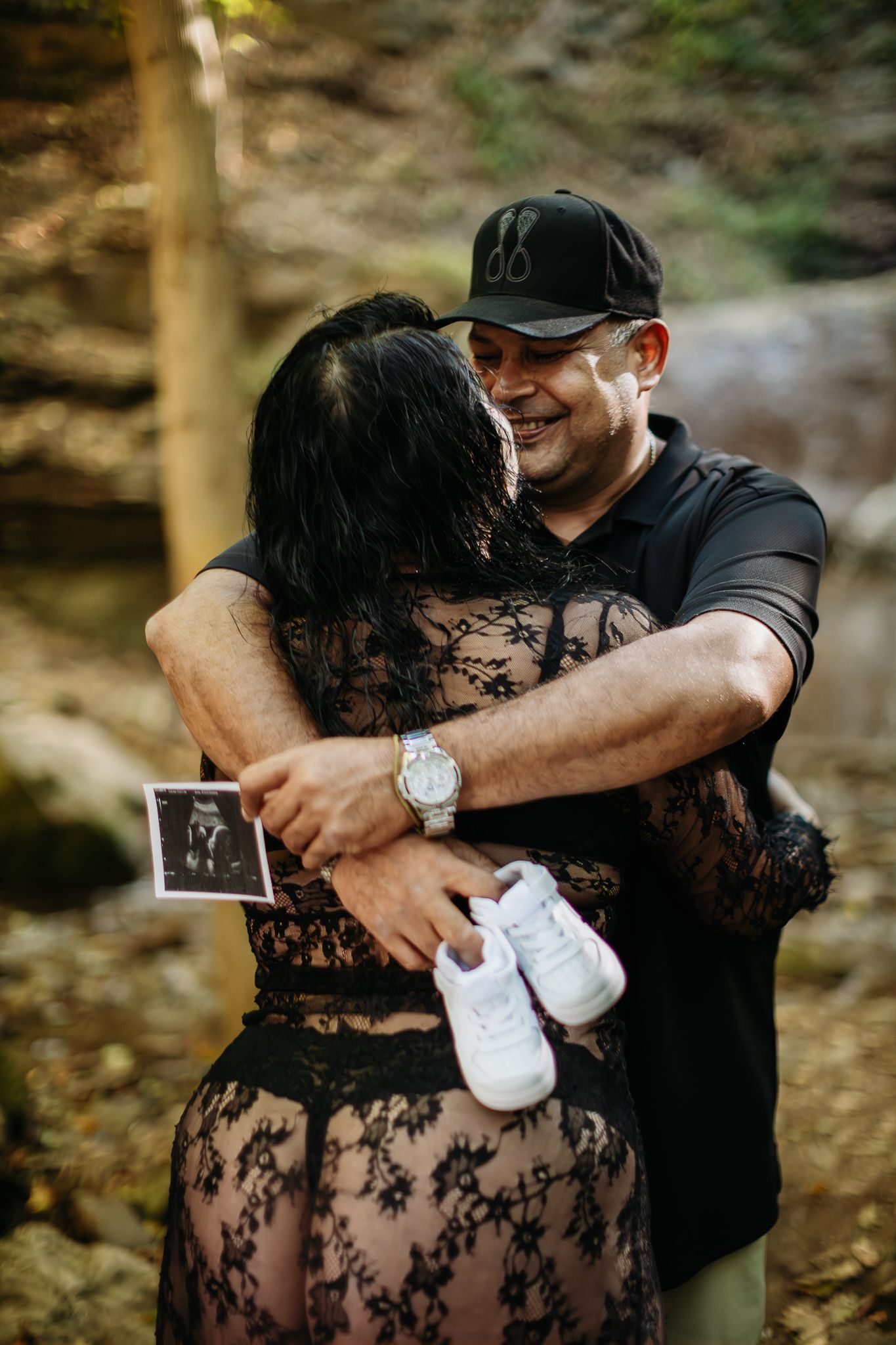 Couple holding ultrasound photos during their pregnancy announcement photoshoot by a waterfall.