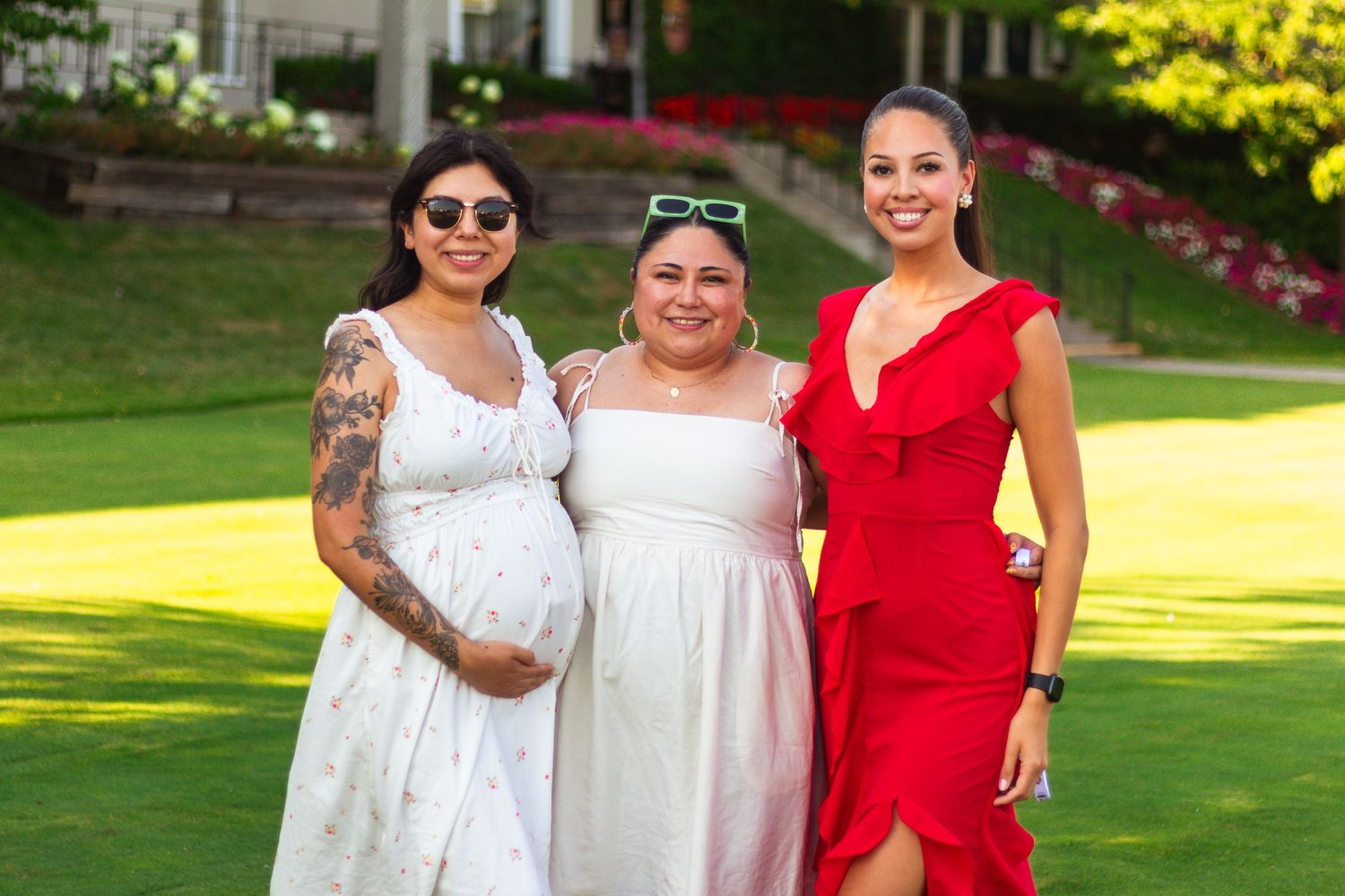 Three people in formal attire posing together on grass during summer event.