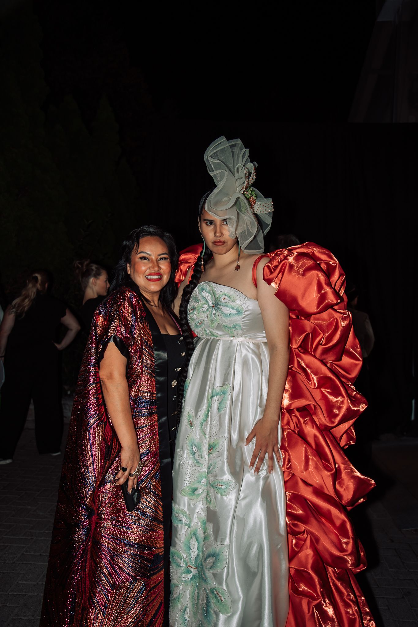 Models pose in dramatic satin evening gowns in mint green, coral, and burgundy colors.