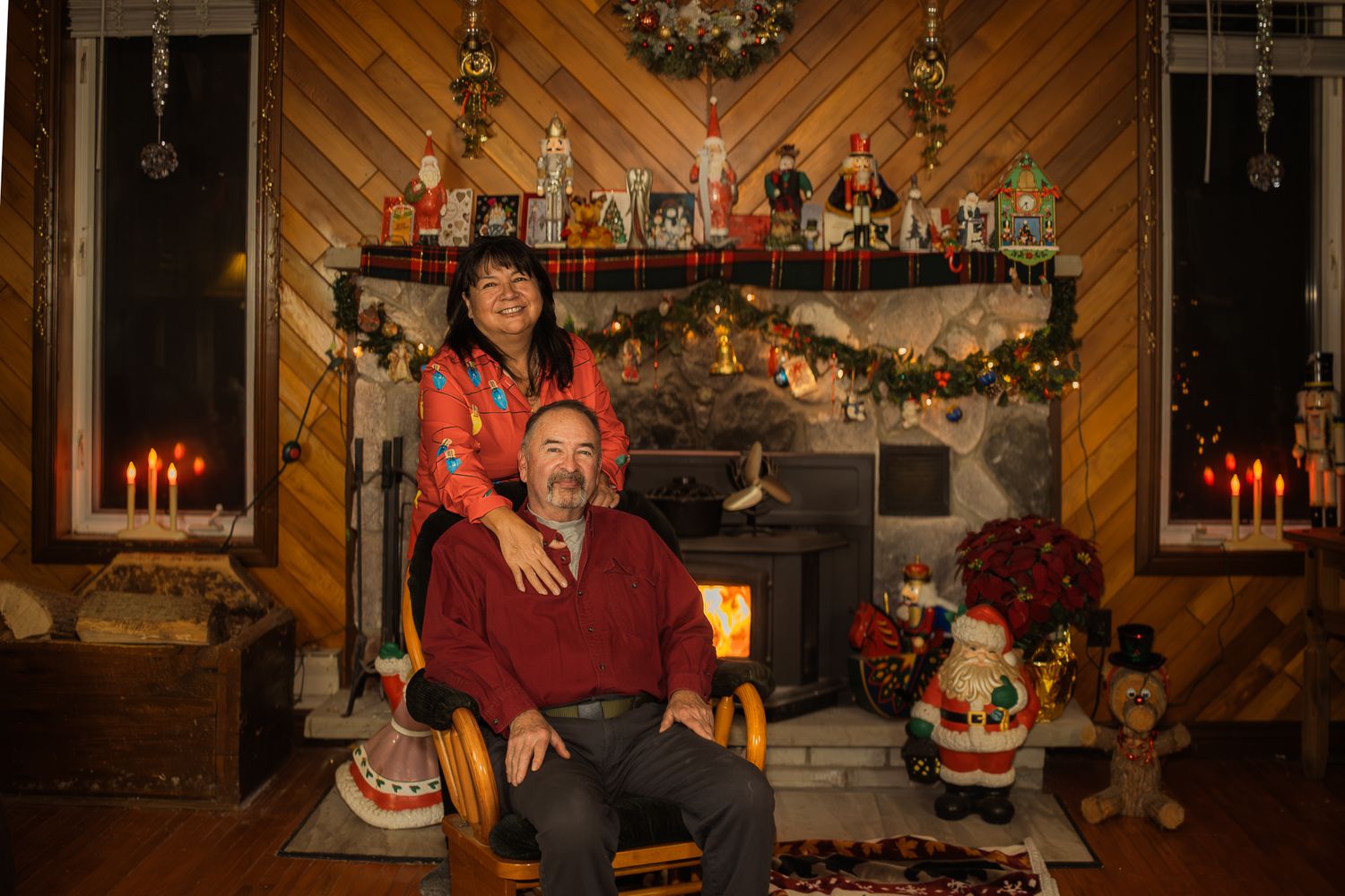 A festive living room with diagonal wood paneling and Christmas decorations displayed around the fireplace.