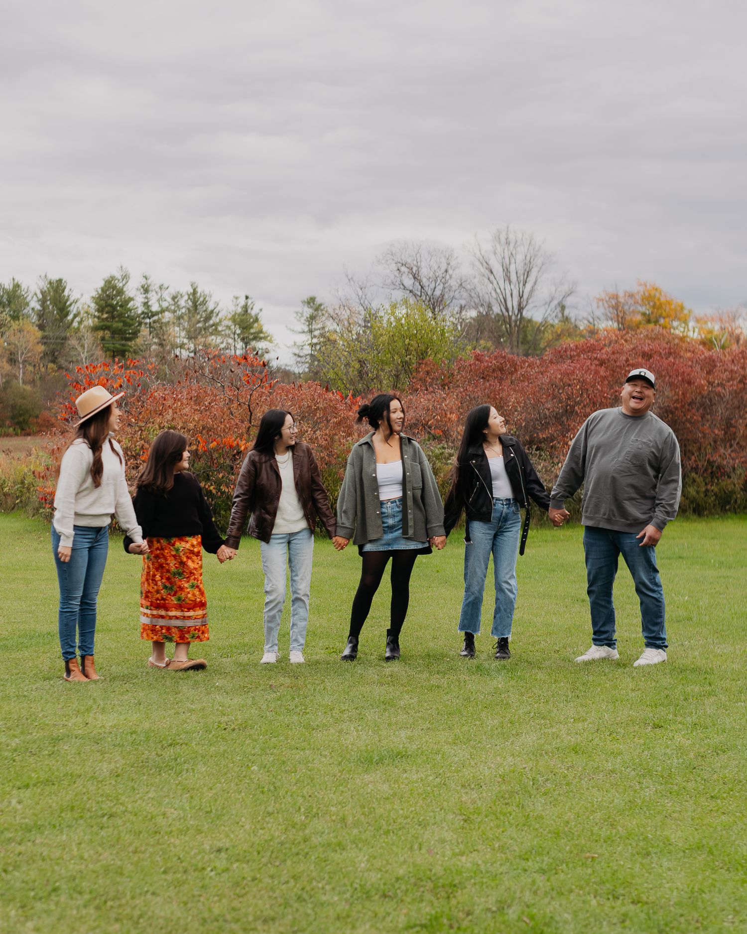 Line of people standing together in a grassy field with autumn colors in the background.