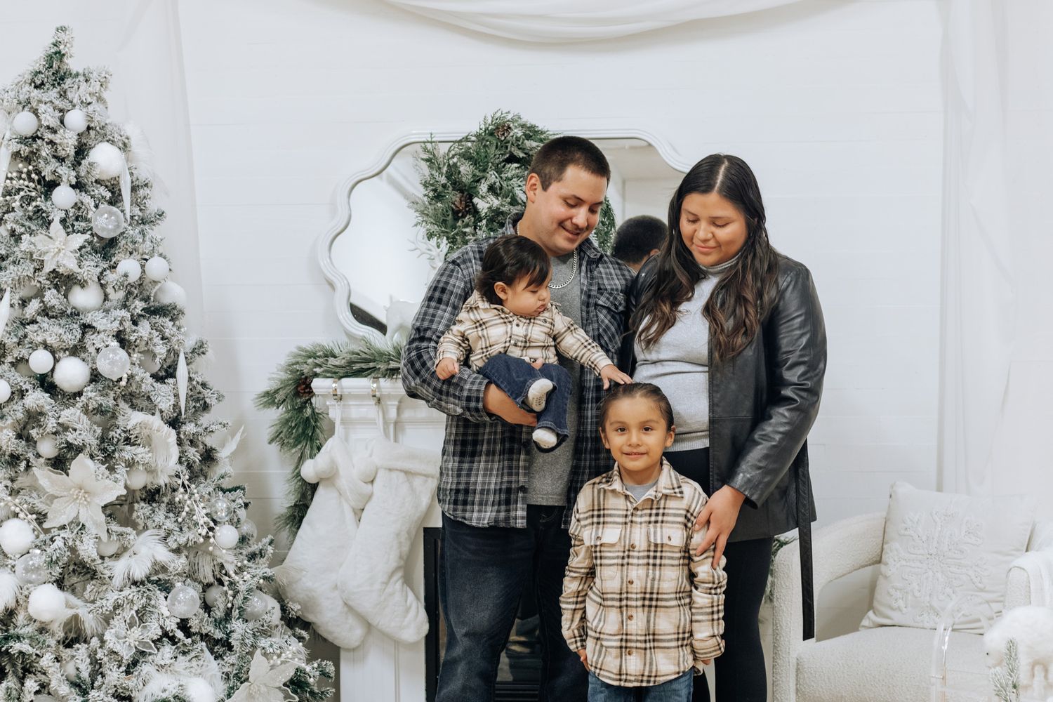 Candid family moment captured during Christmas photo session with decorated white trees.
