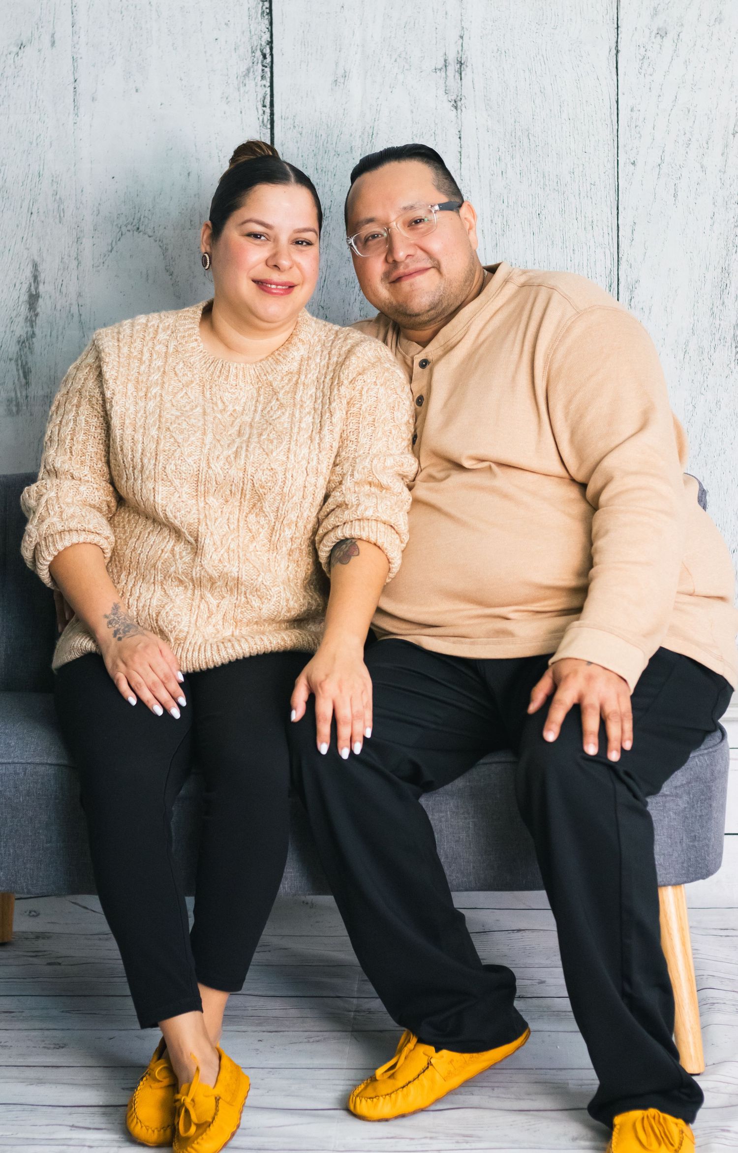 Couple in coordinated cream outfits and yellow shoes sitting together against white backdrop.