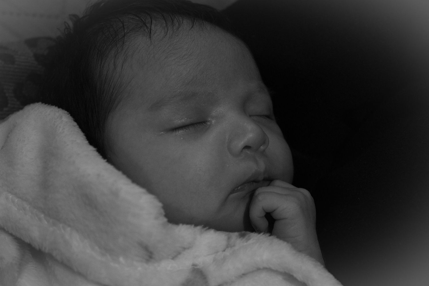 Close-up black and white portrait of a sleeping newborn baby in soft focus.