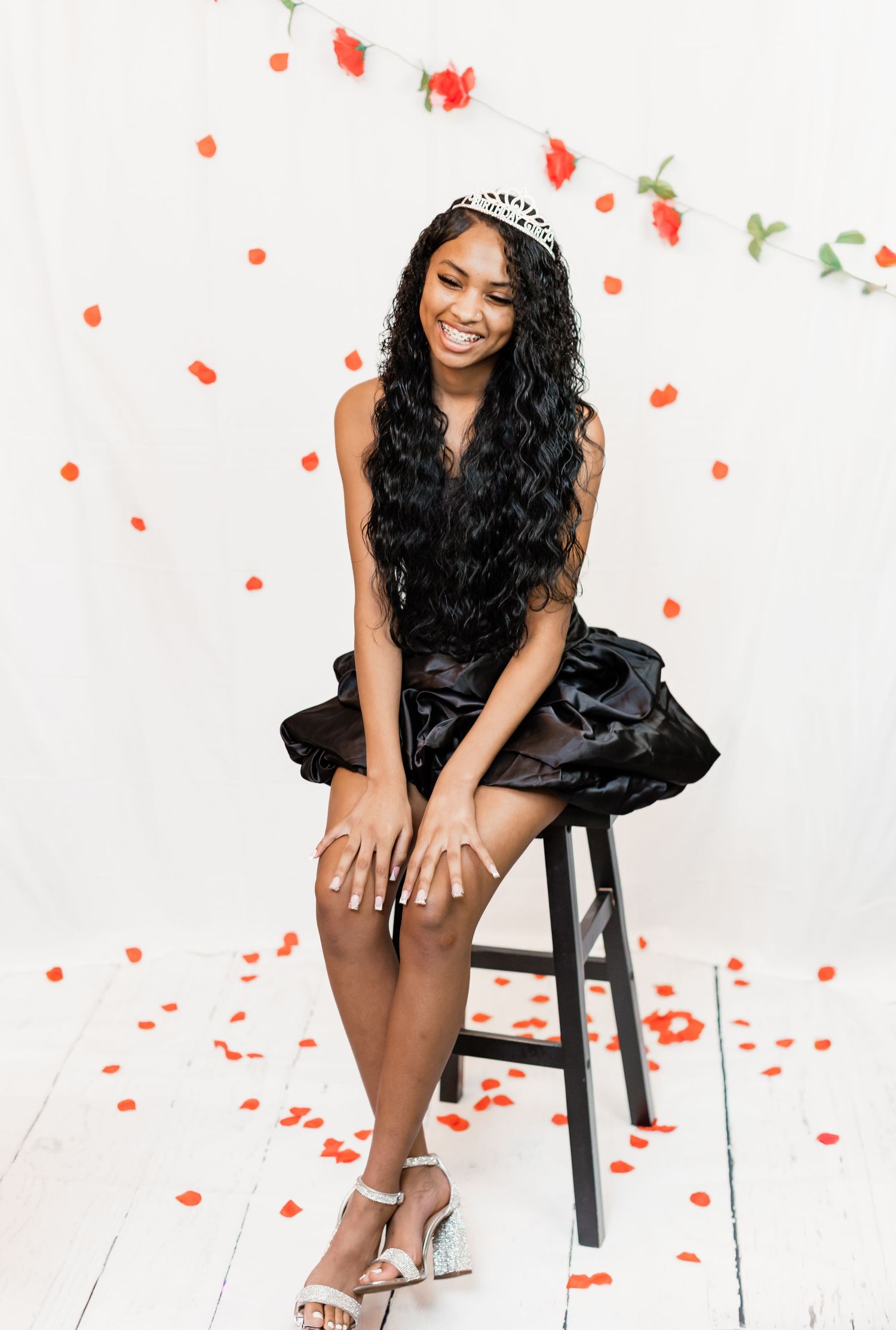 Glamorous photo shoot with scattered red rose petals and formal black dress.