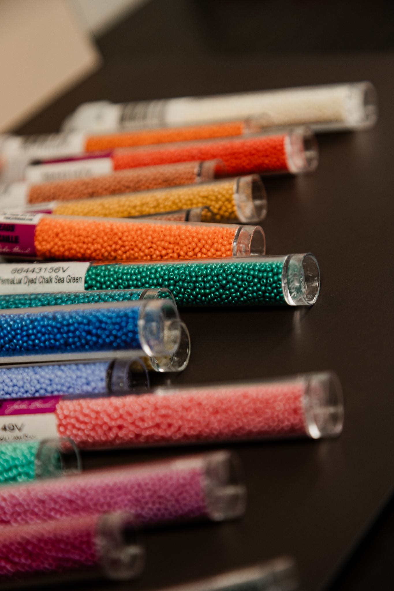 Colorful seed beads in clear plastic tubes arranged on a dark surface, perfect for jewelry making and crafting projects.