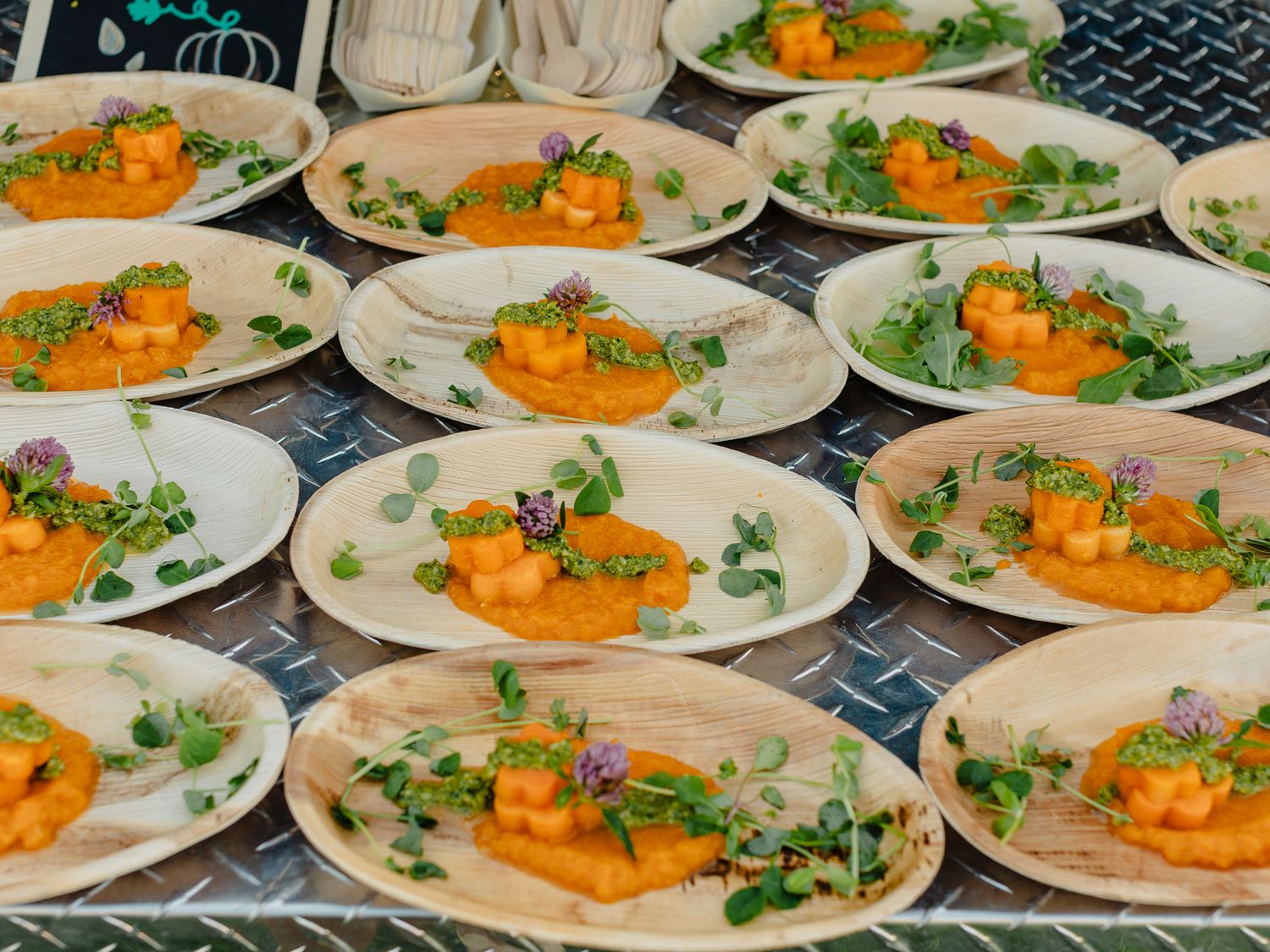 Elegant plated dishes with orange puree, fresh microgreens, and edible flowers arranged on rustic palm leaf plates.