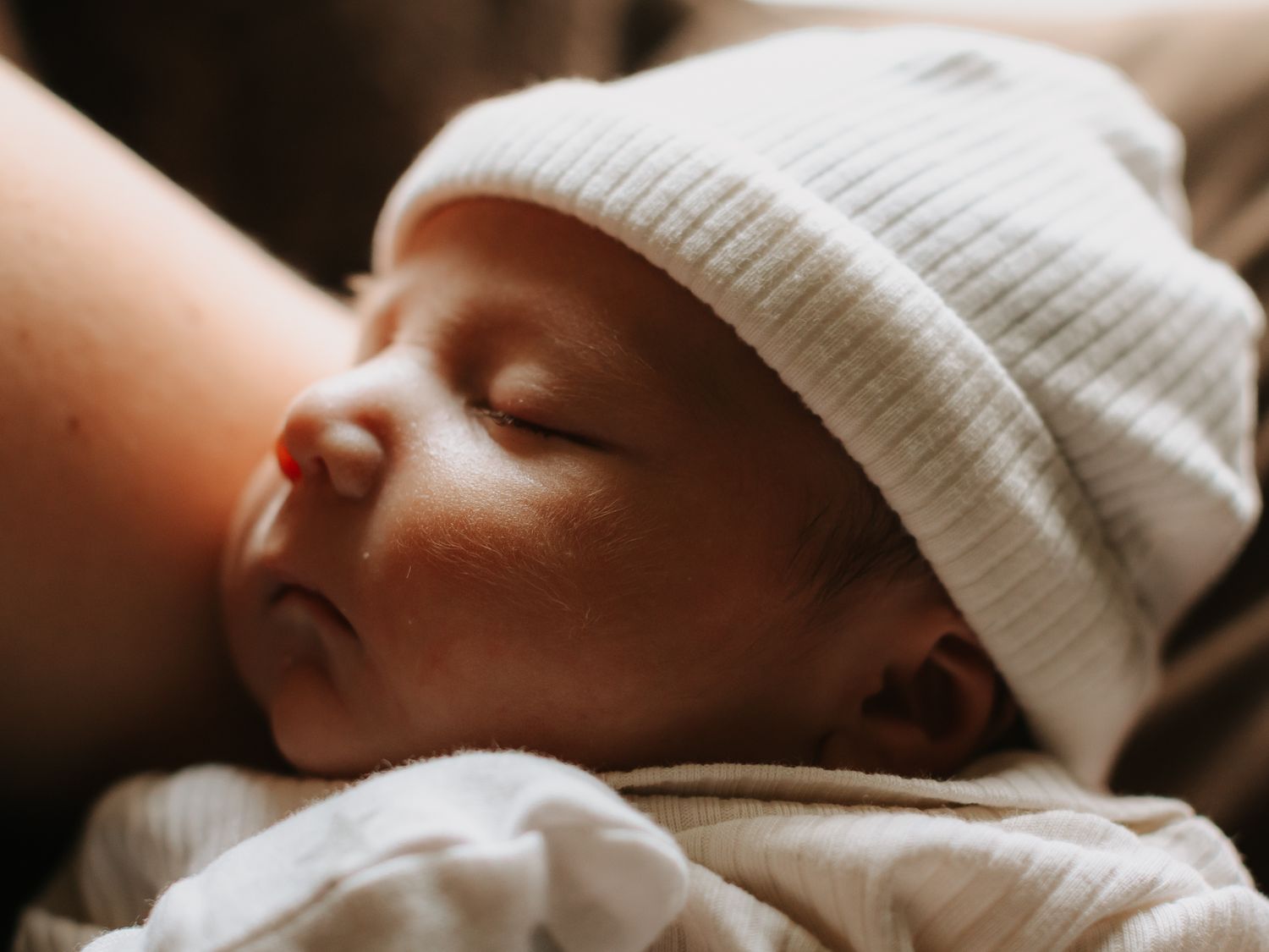 A peaceful newborn baby sleeping in a white knit hat, cradled in loving arms after birth.