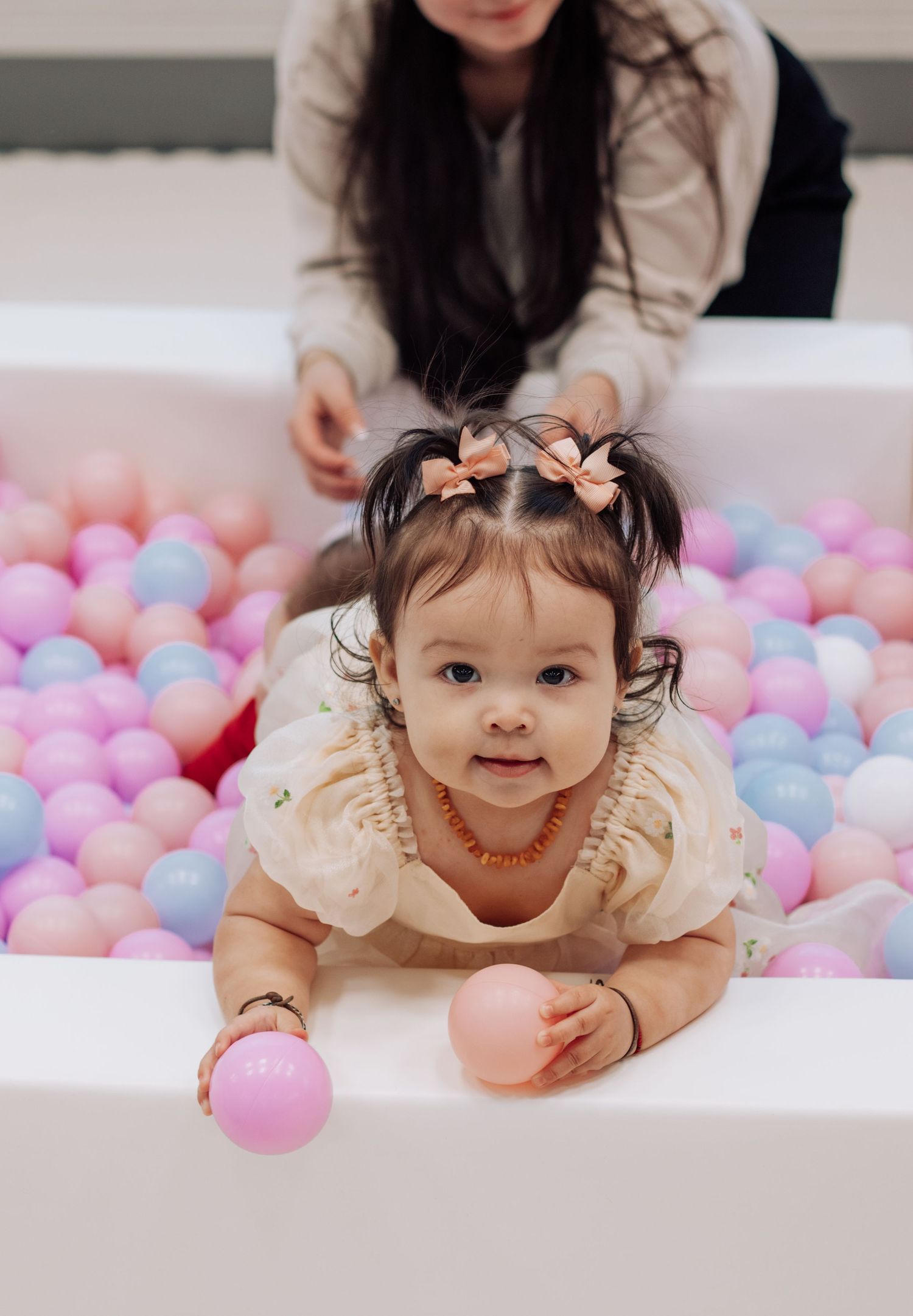 Baby playing in pink and blue ball pit during birthday celebration.