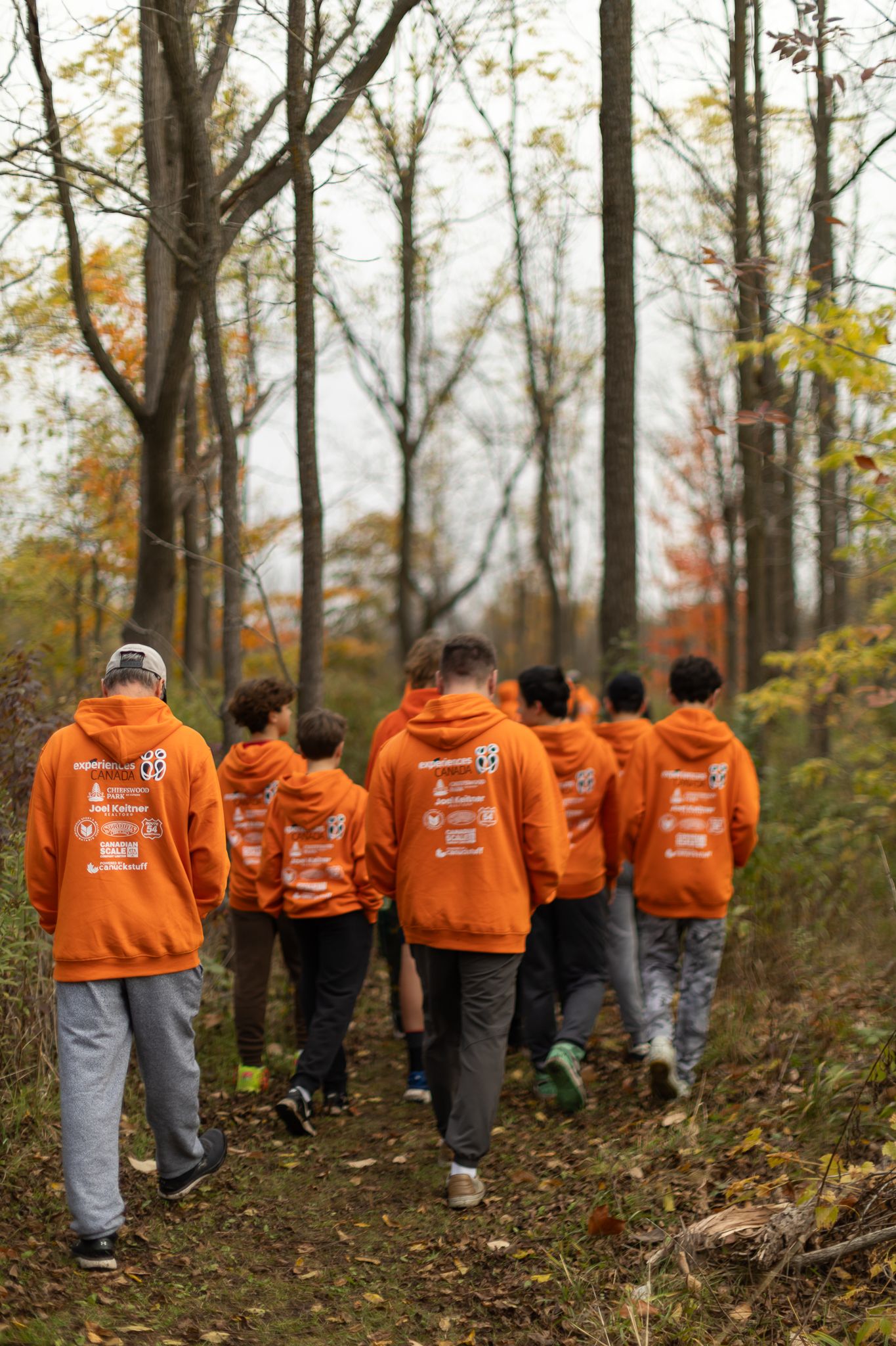 Group walking through autumn woods wearing matching orange hoodies.