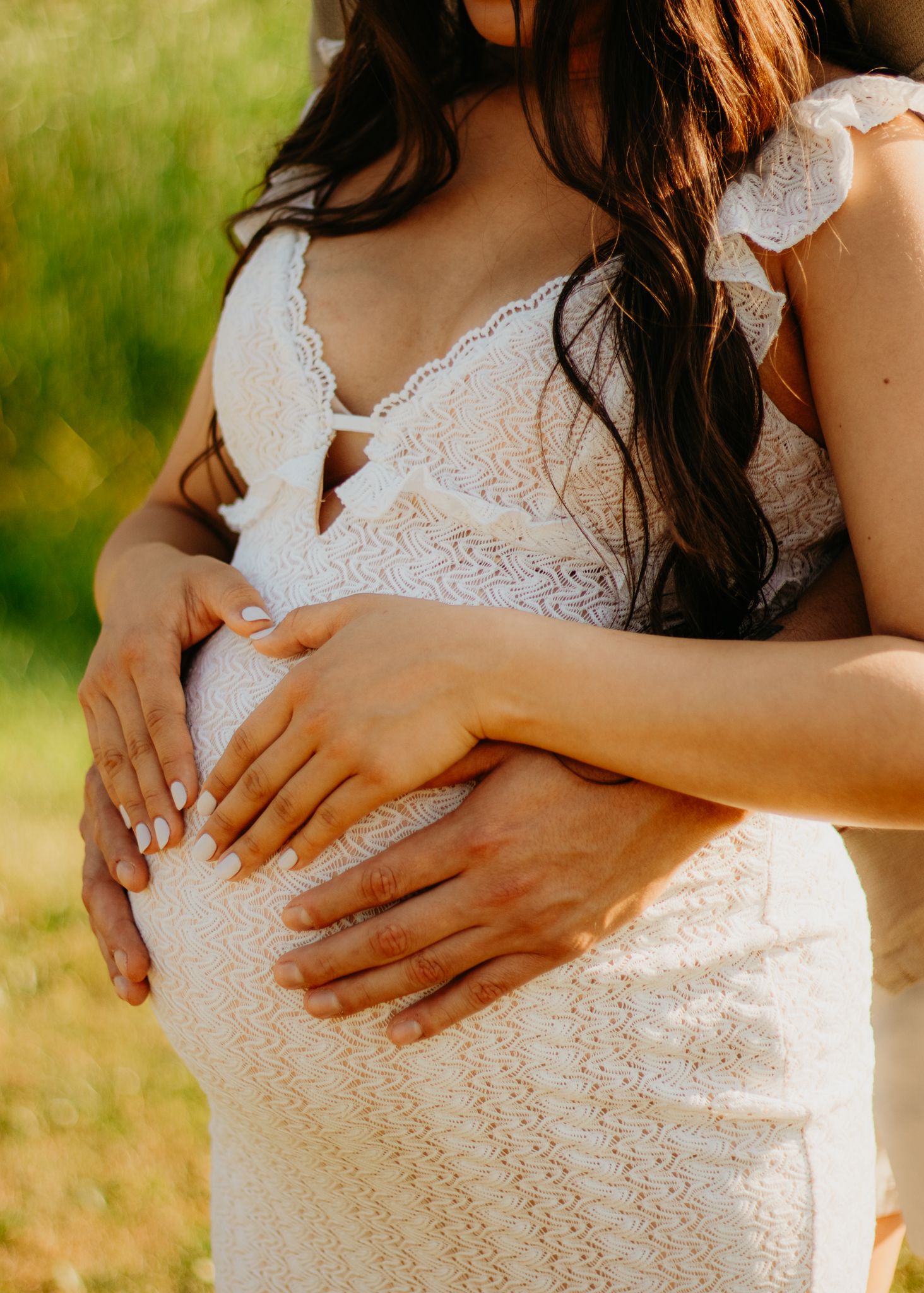 Close-up shots of hands tenderly cradling a pregnant belly in a white lace dress.