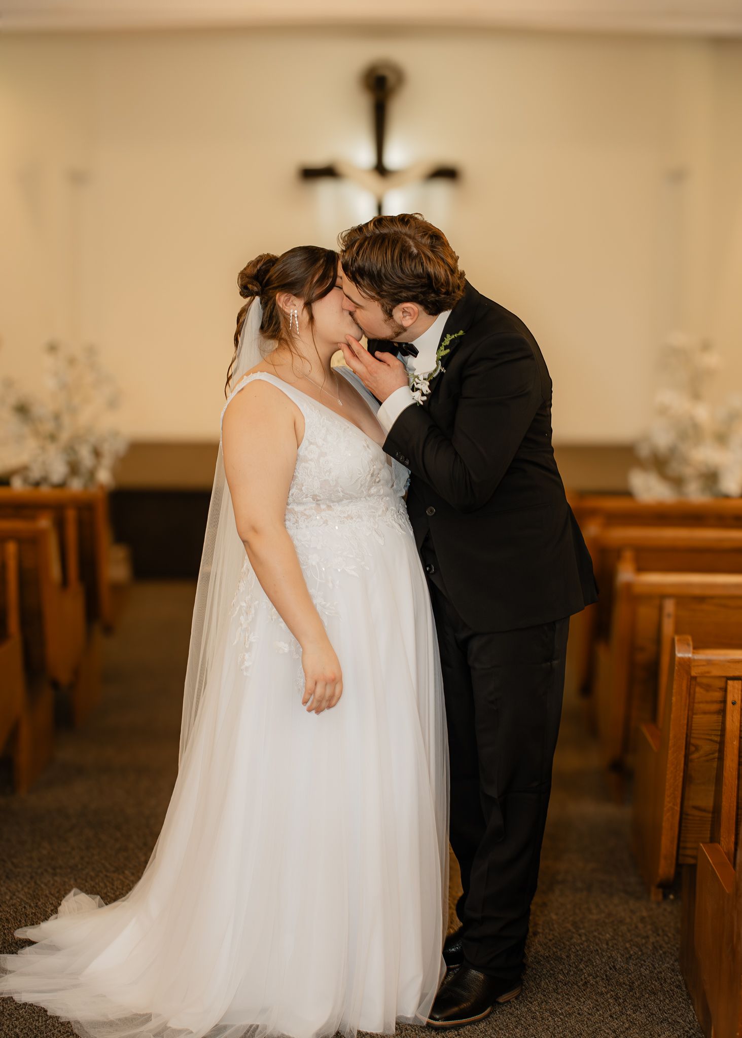 Bride and groom share a tender forehead kiss in church aisle after wedding ceremony.