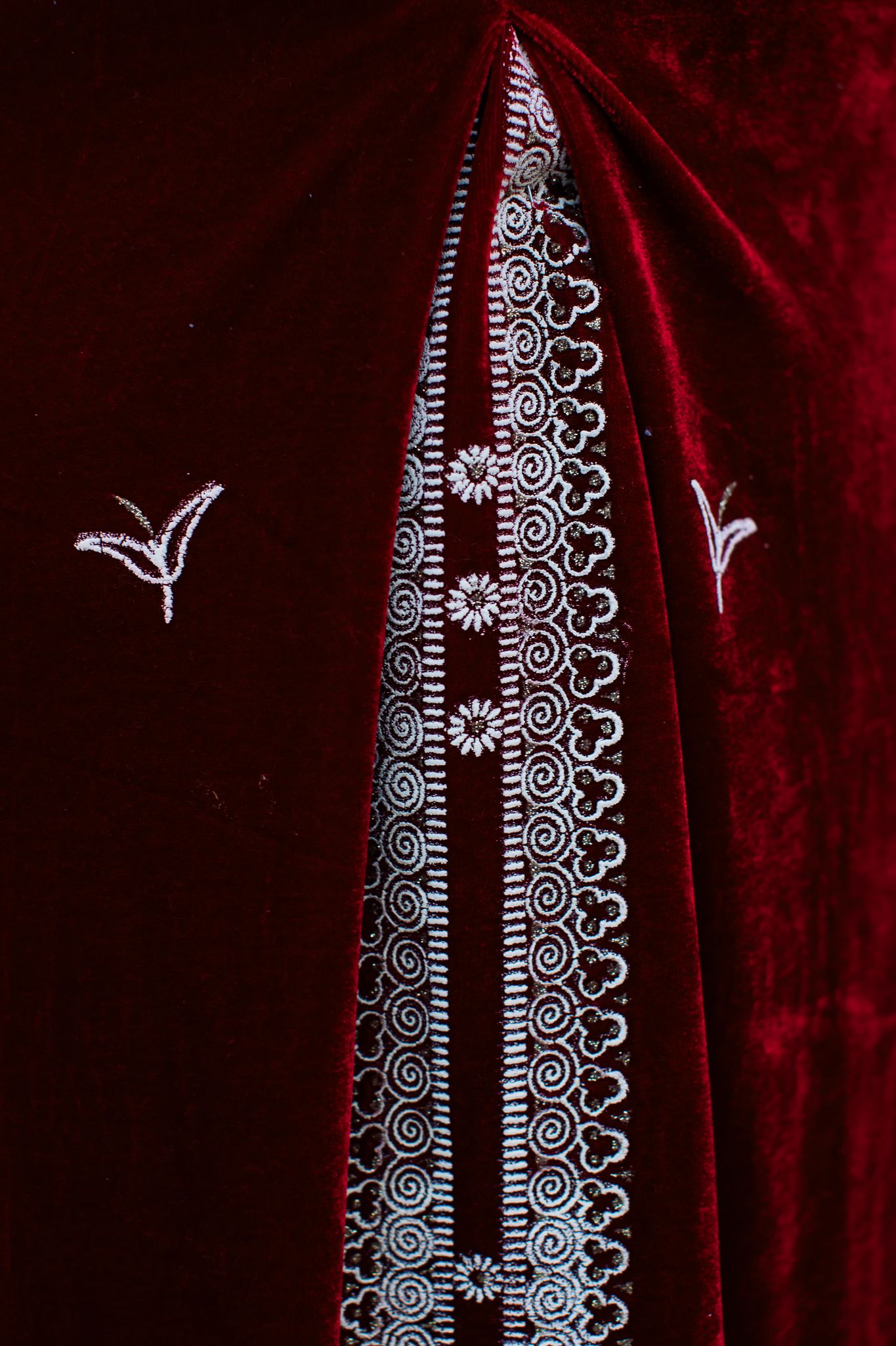 Deep red velvet fabric with intricate silver embroidery and floral details.