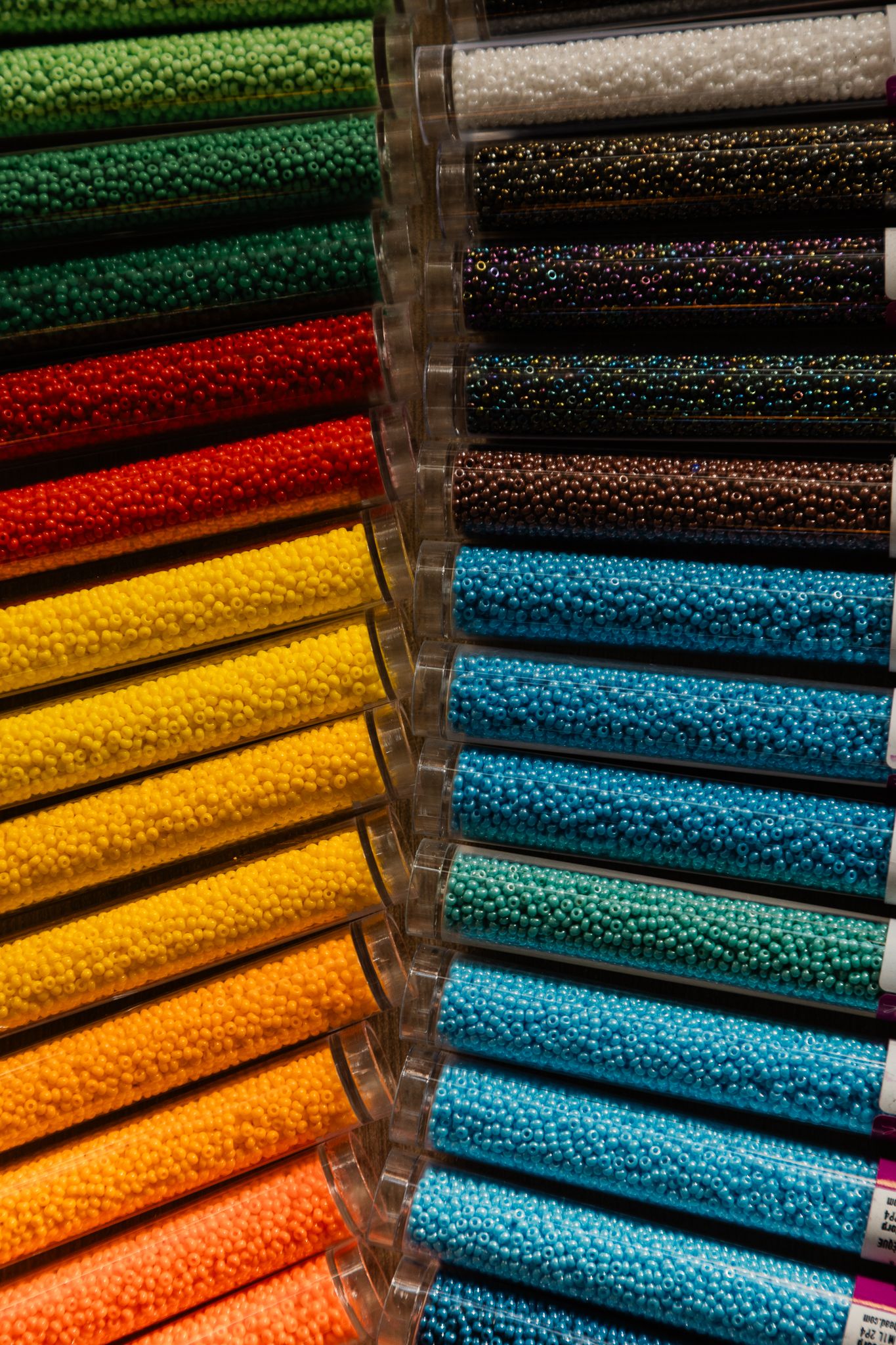 Colorful seed beads in tubes arranged in a rainbow spectrum display, perfect for crafting and jewelry making.