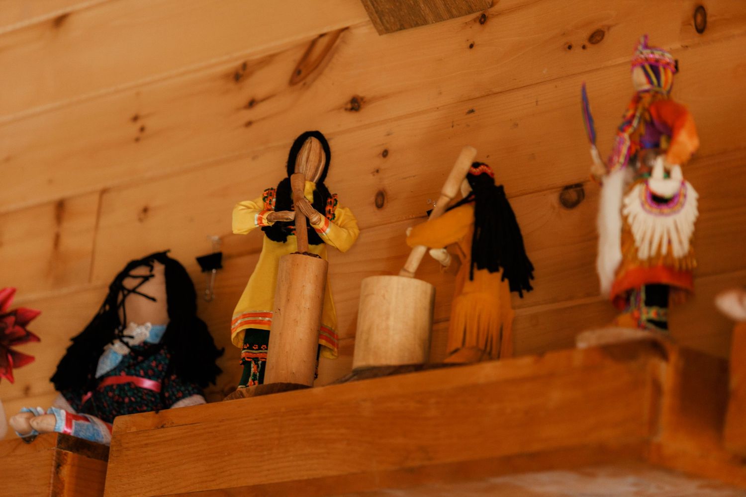 Traditional Indigenous handmade dolls and figurines displayed on a wooden shelf in a log cabin.