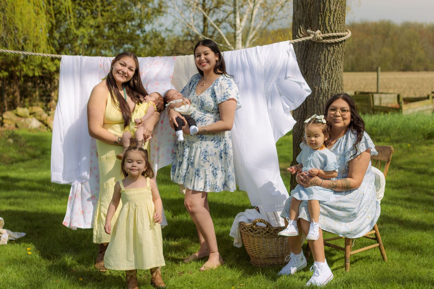 Three women and two young children pose outdoors by a clothesline with white laundry on a sunny spring day.
