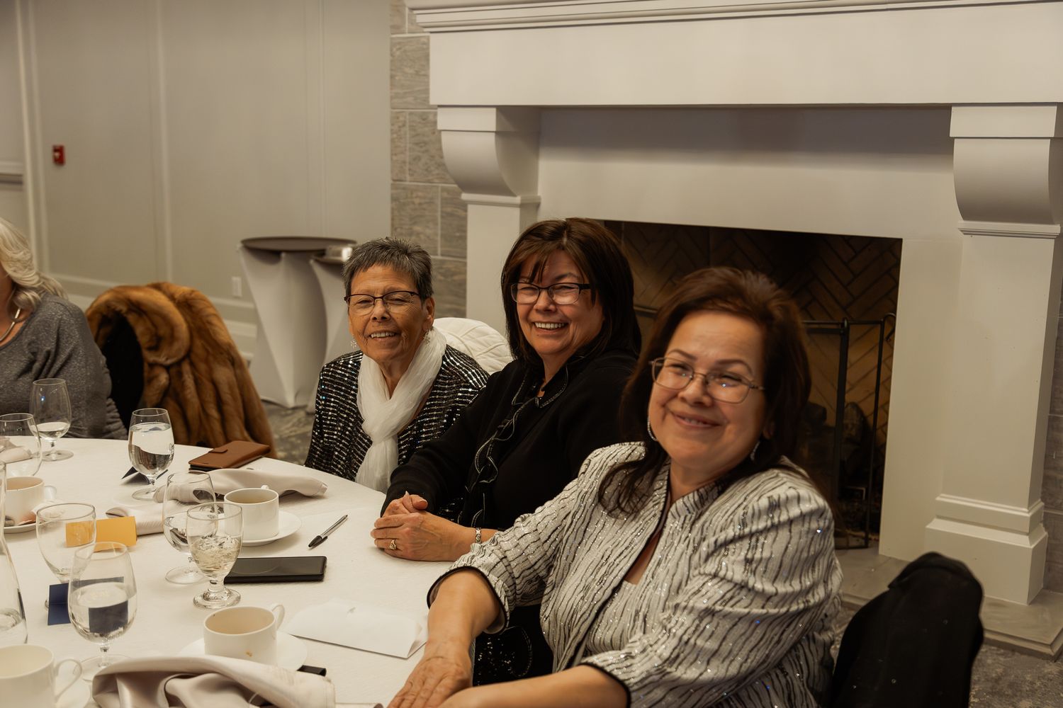 Guests seated at a dining table near a white fireplace during an indoor event.