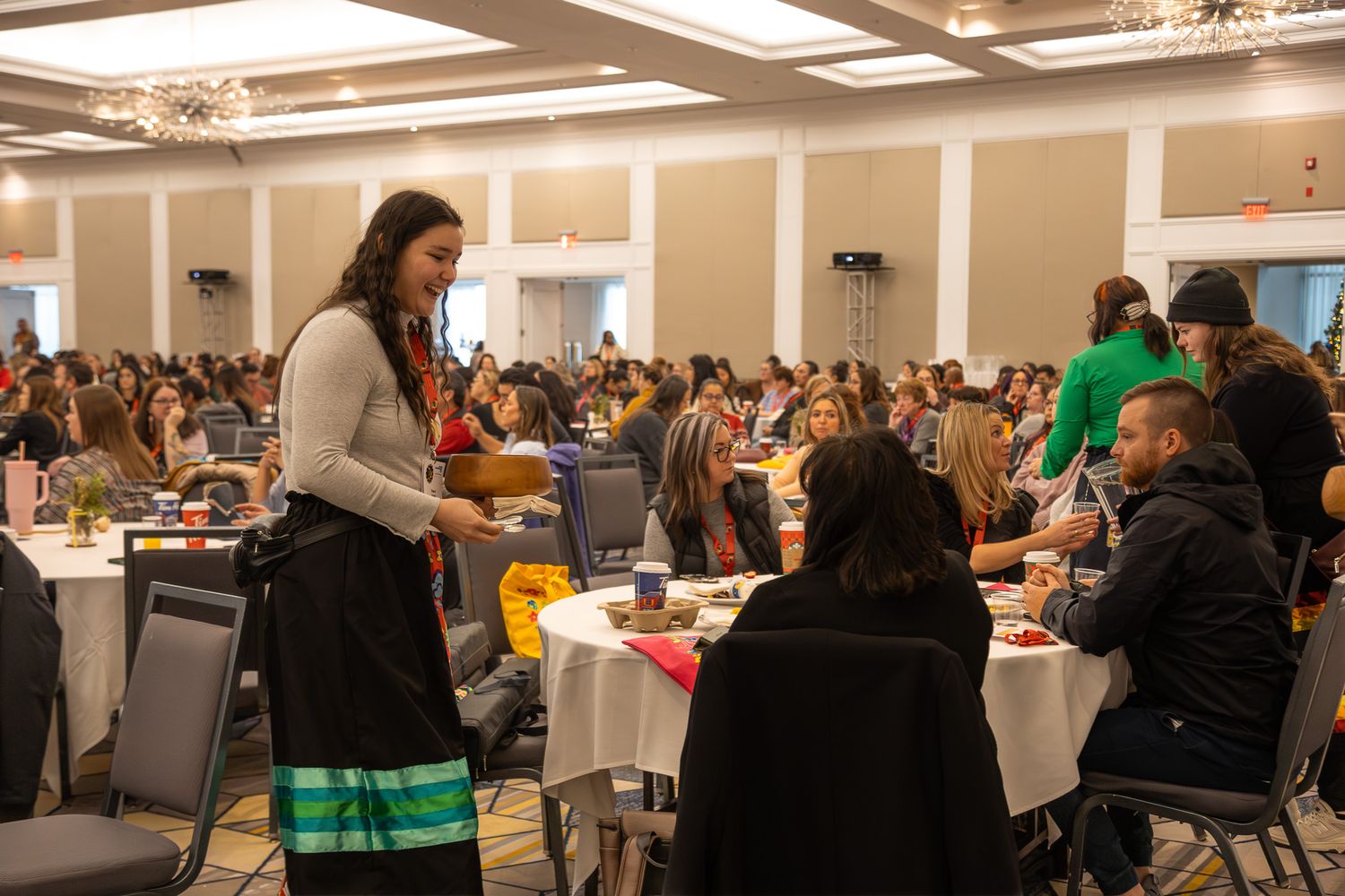 Large conference room filled with attendees seated at round tables during a professional event.