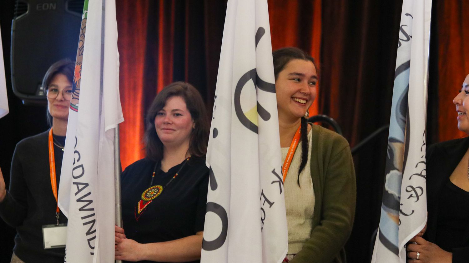 Standing banners and flags line up against a dark background at a conference venue.