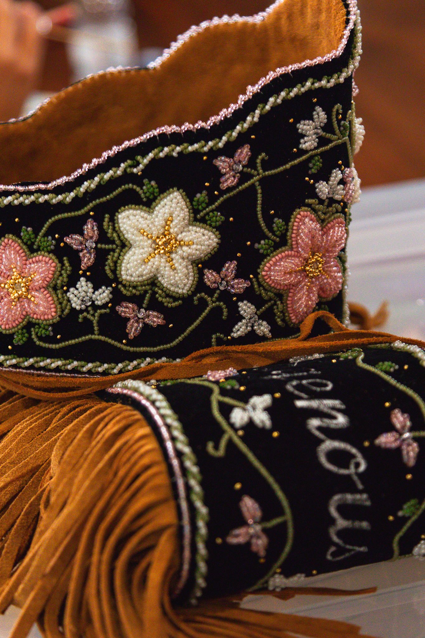 Detailed beadwork and embroidered floral design on black and brown leather with fringe.