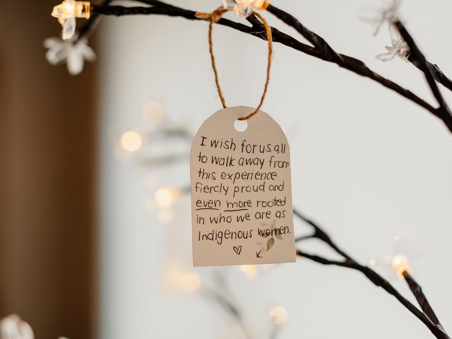 Wooden tag ornament with an inspiring Indigenous women empowerment quote hanging on a lit branch.