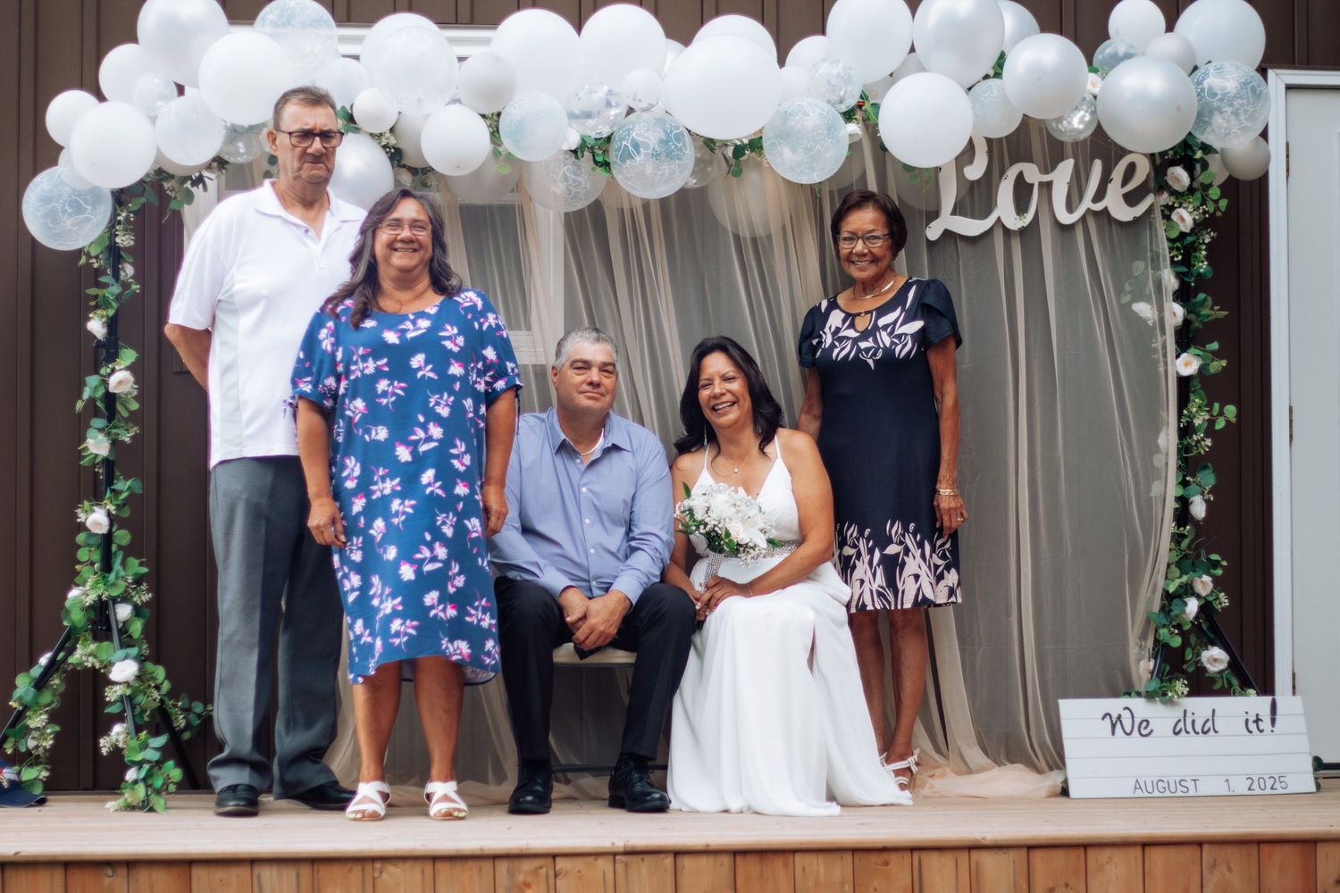 Wedding party group photo with bride holding bouquet under Love balloon arch decoration.