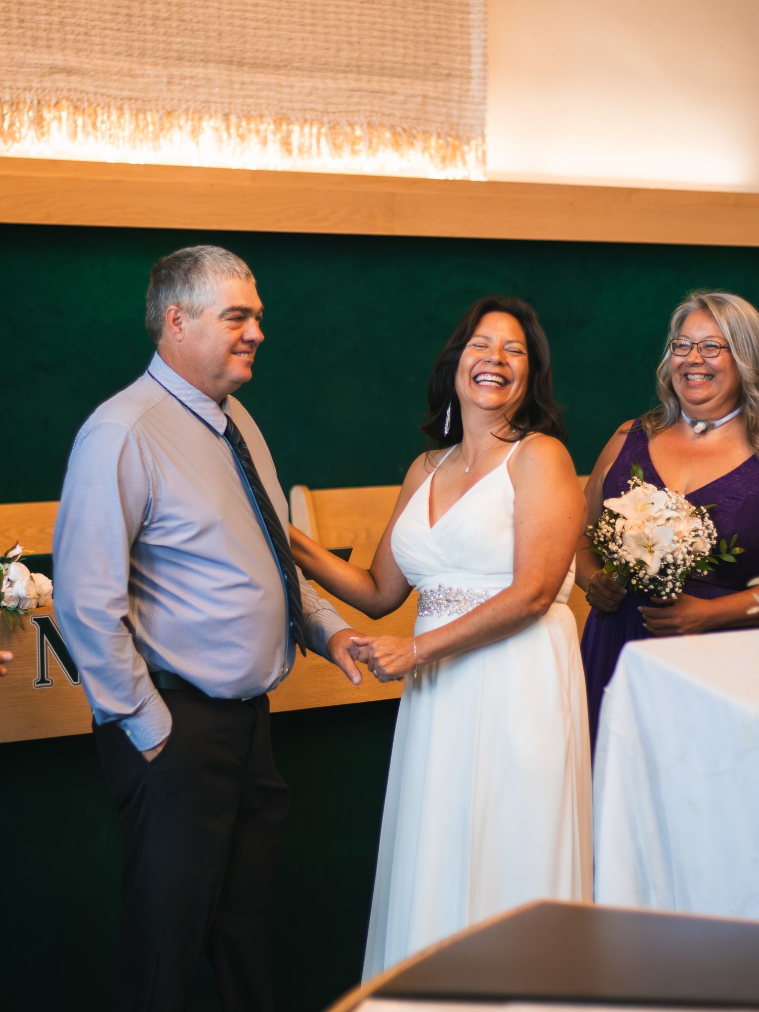 Bride laughing joyfully with groom and officiant during intimate indoor wedding ceremony.