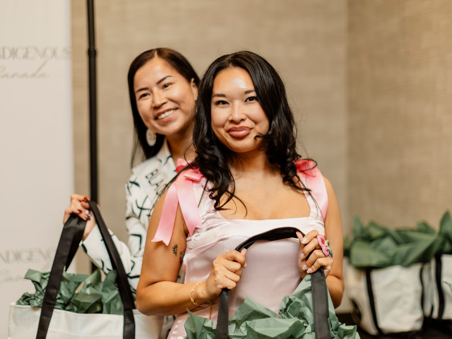 Two smiling women holding floral tote bags at an Indigenous Canada event.