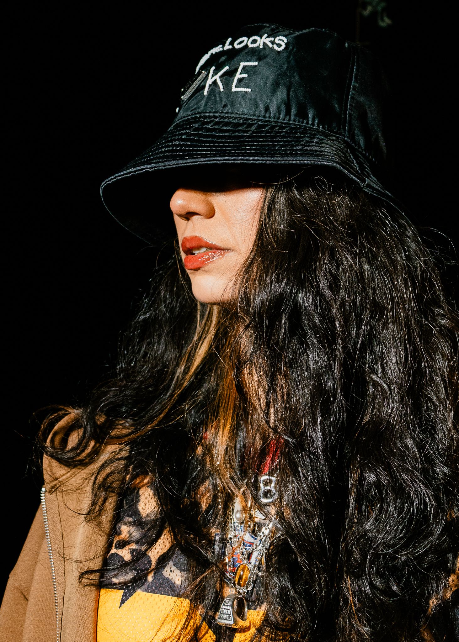 Woman in black bucket hat and yellow top with layered necklaces poses in sunlight.
