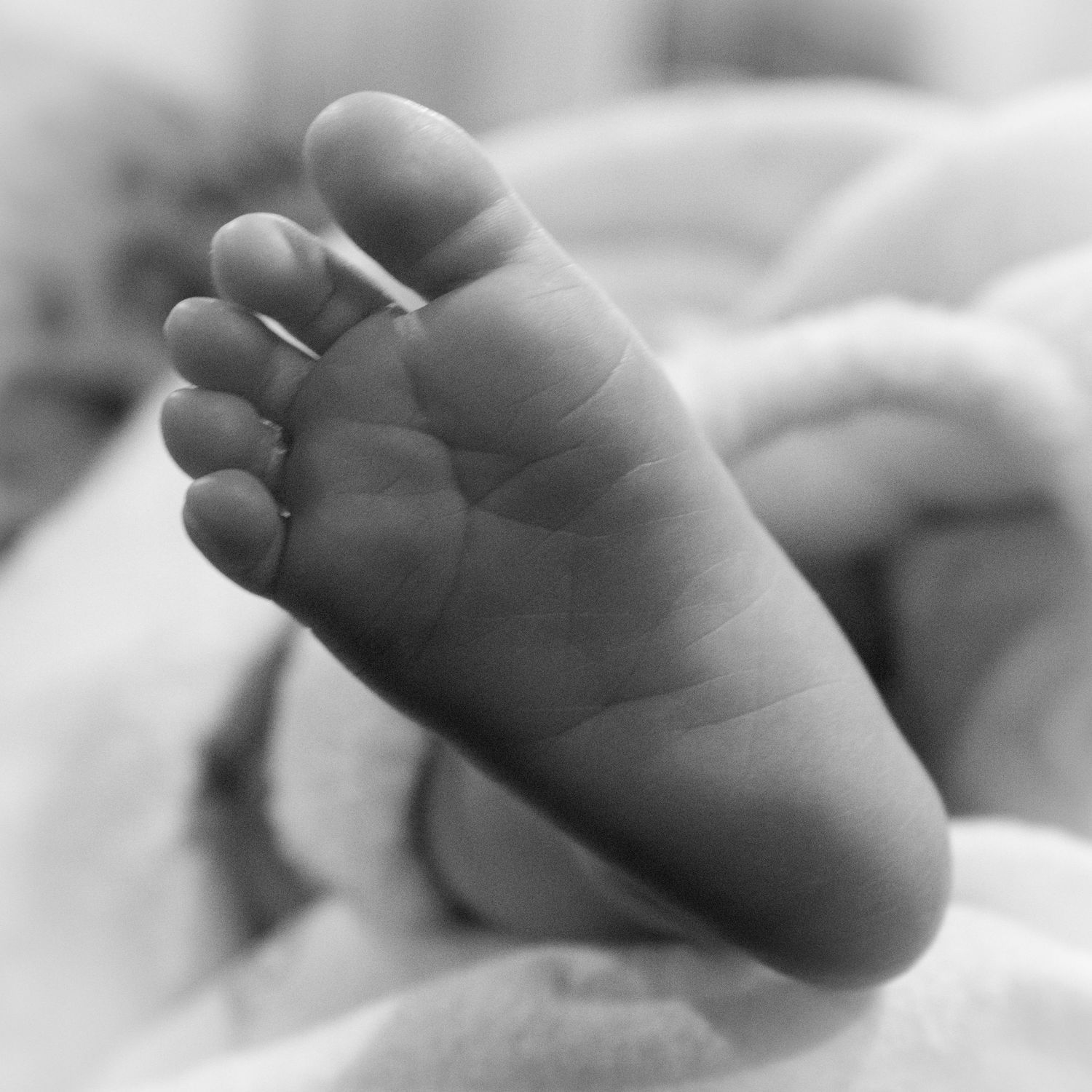 Delicate tiny baby feet against white bedding in monochrome photography.