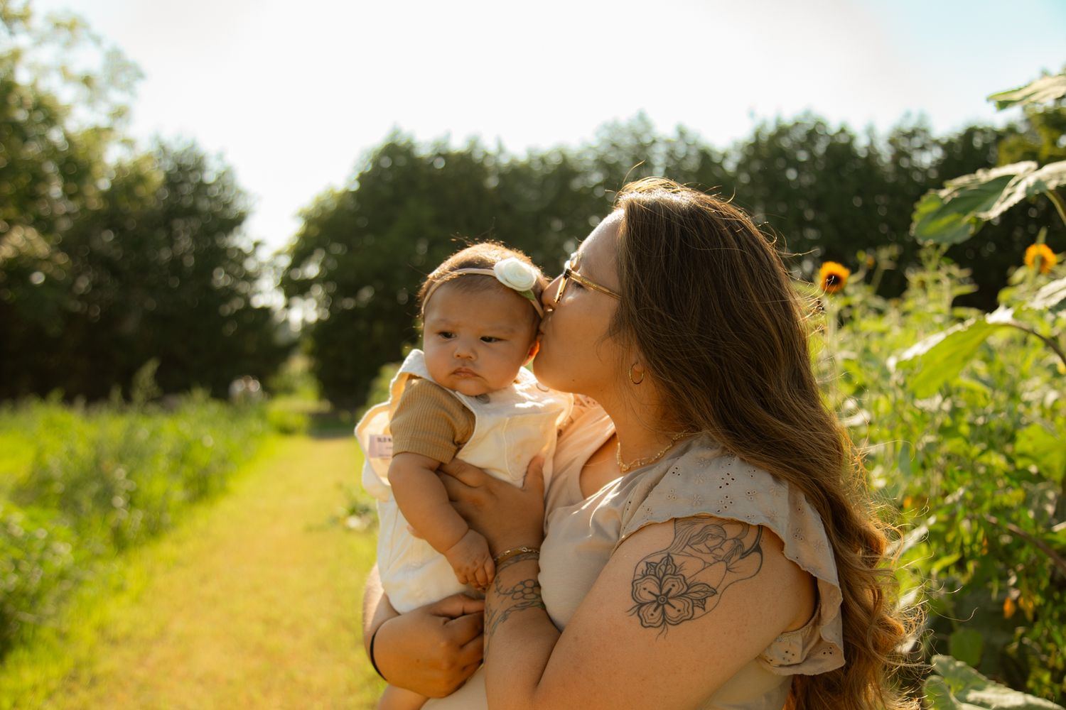 Tender moment captured between parent and baby in golden summer sunlight.
