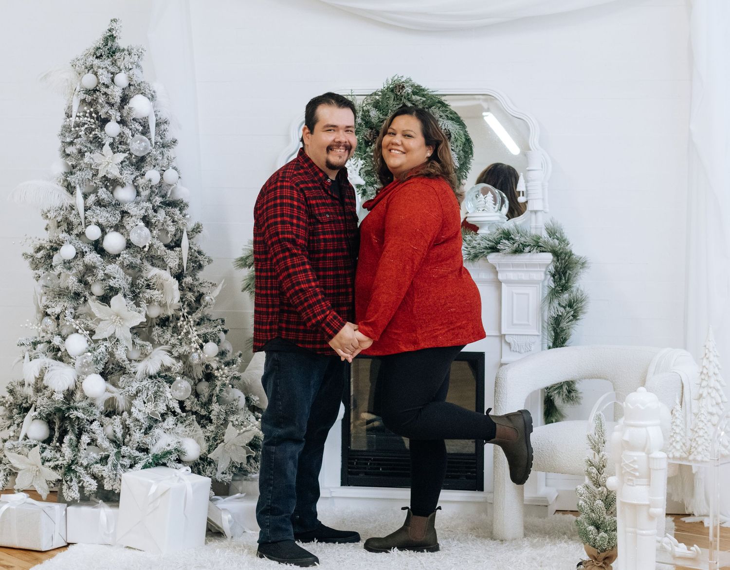 Holiday portrait of couple in matching red and plaid outfits by Christmas tree.