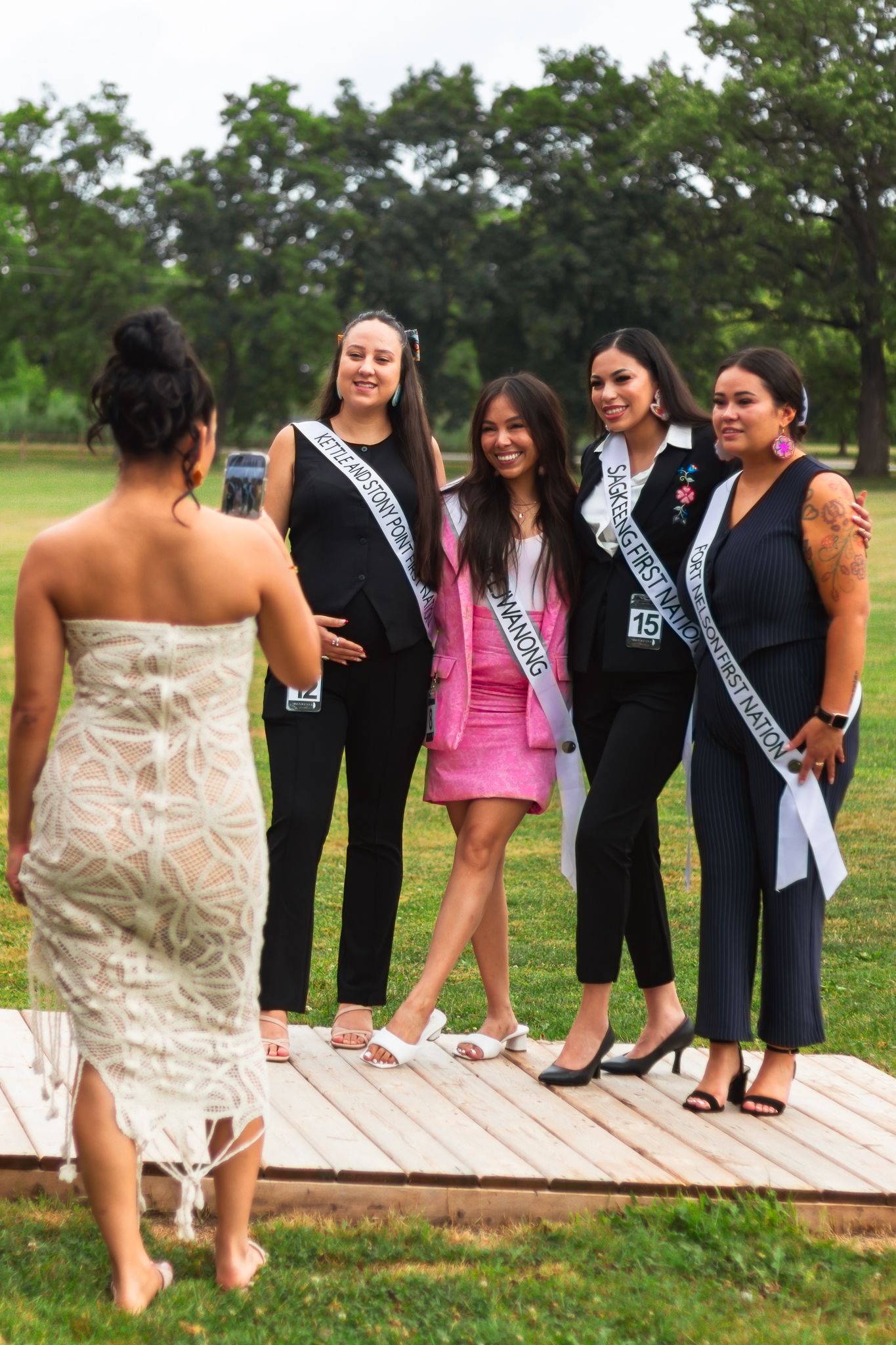 A group in formal attire poses on a wooden deck during an outdoor event.
