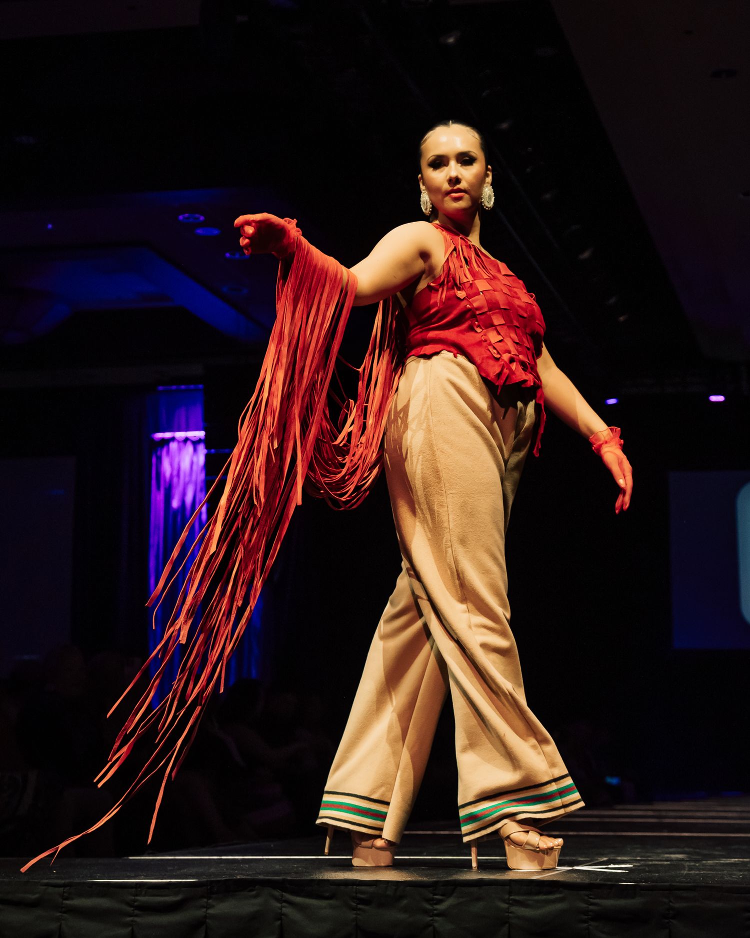 Dancer with red hair extensions performing in beige outfit on dark stage.