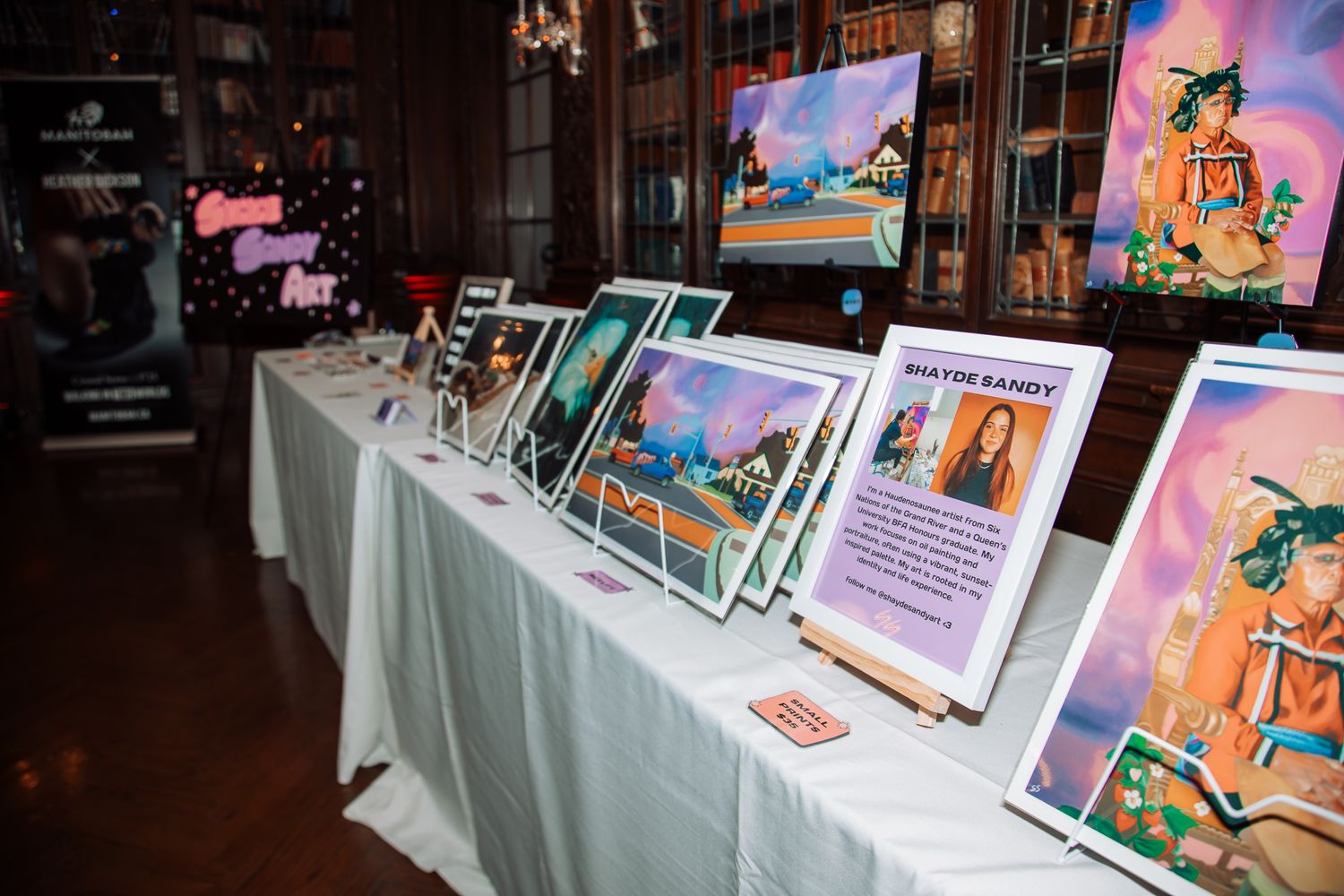 Art prints and photographs displayed on white tables at an exhibition or gallery event.