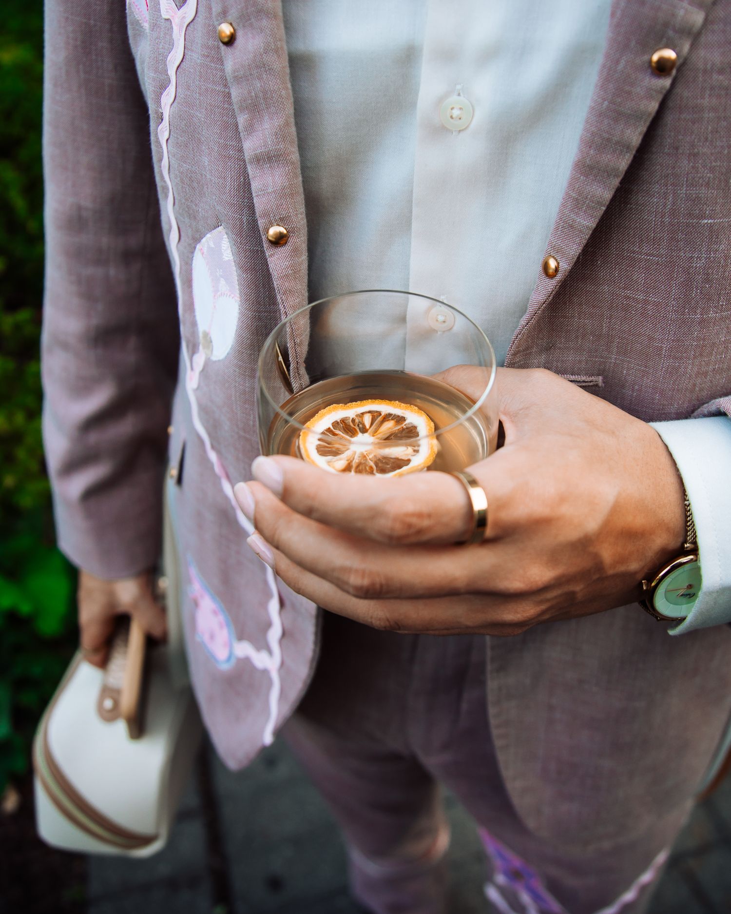 Close-up of hands holding a cocktail glass garnished with a dried lemon slice at an outdoor event.