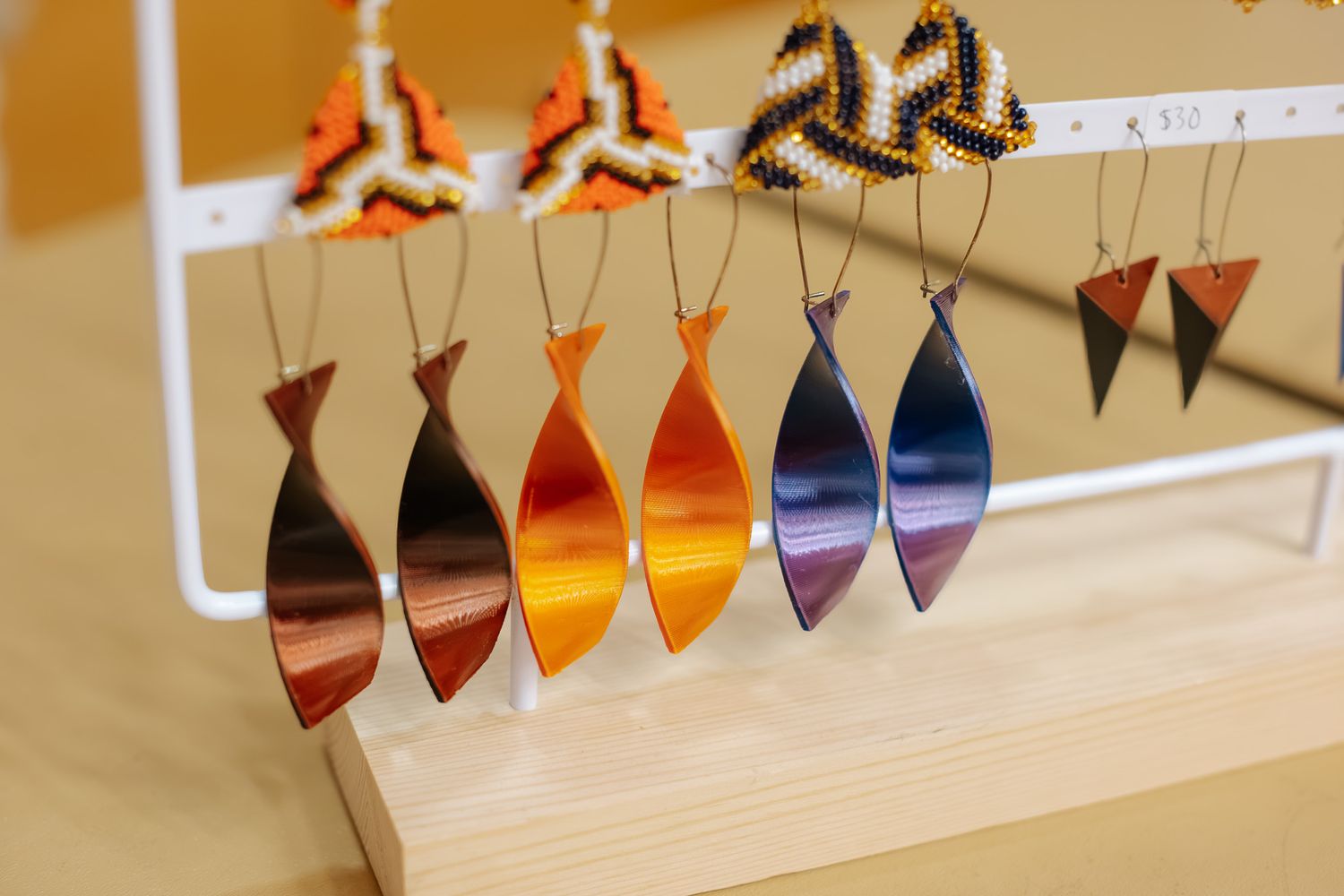 Colorful fish-shaped and triangle earrings displayed on a white jewelry stand, featuring orange, purple, and brown tones.