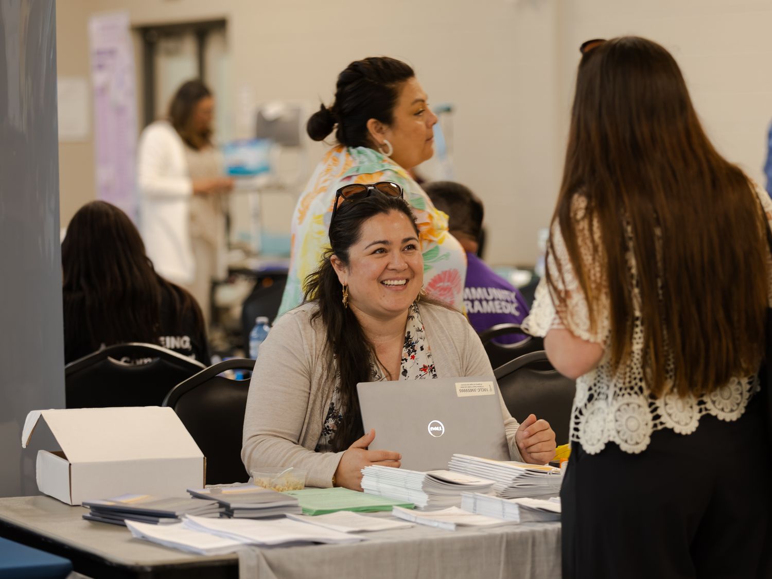 Smiling woman with laptop assists visitor at a community health event registration table.