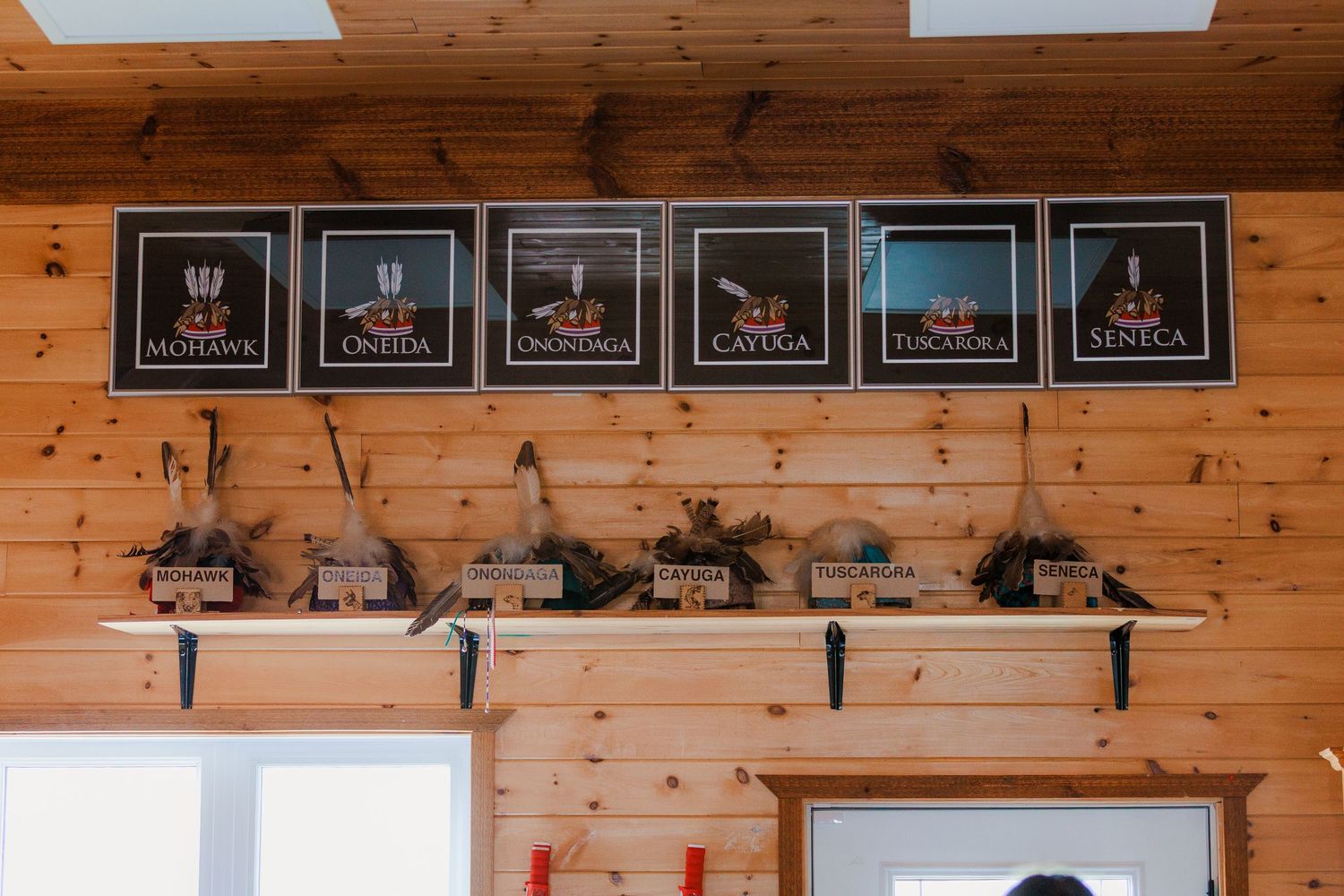 Iroquois Six Nations Haudenosaunee tribal signs displayed on wooden wall with artifacts on shelf below.