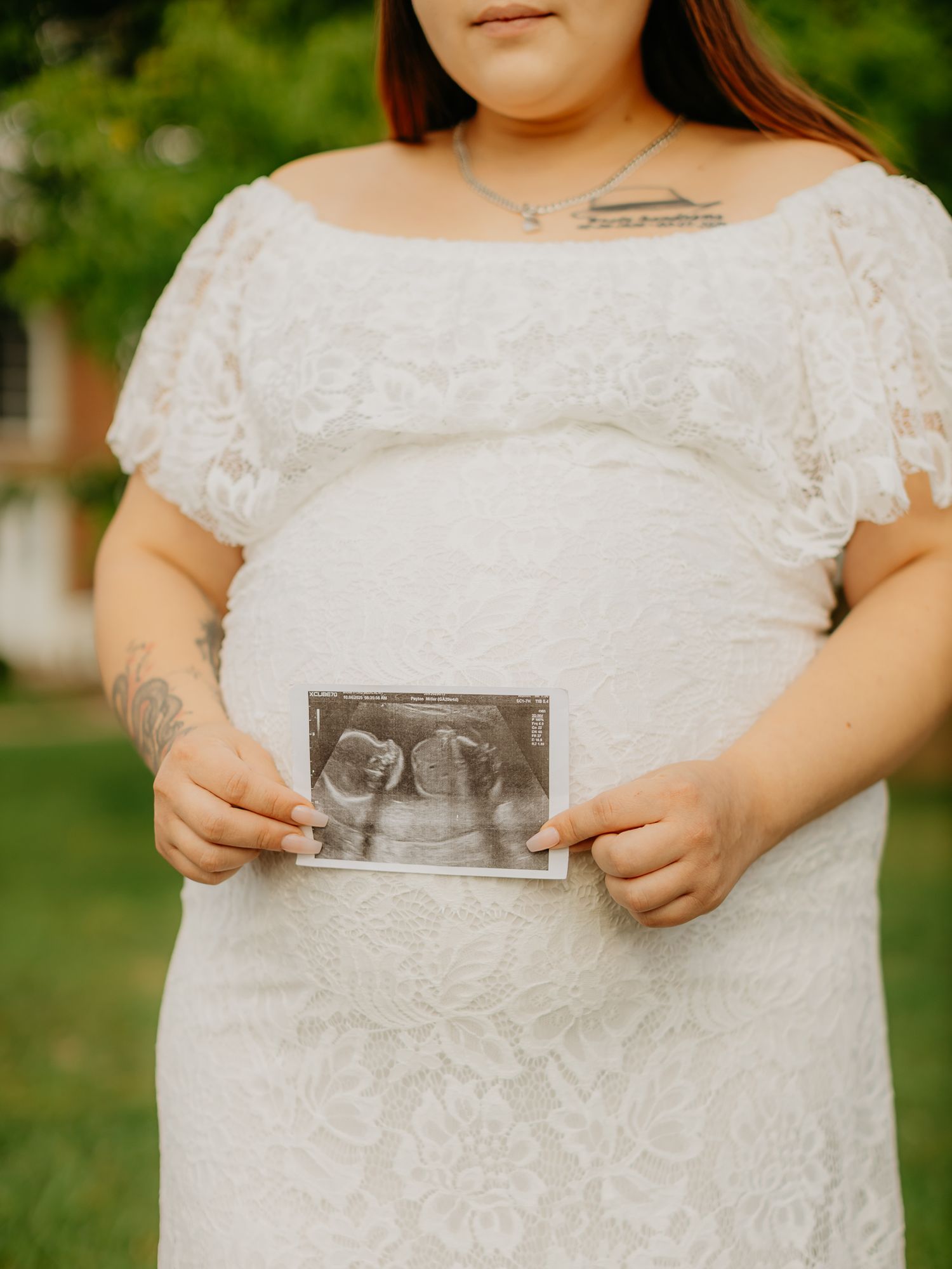 Someone in a lace dress holds up an ultrasound photo during a maternity shoot.