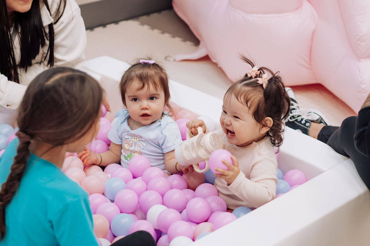 Children enjoying a playful moment with pink and purple balloons on the floor.