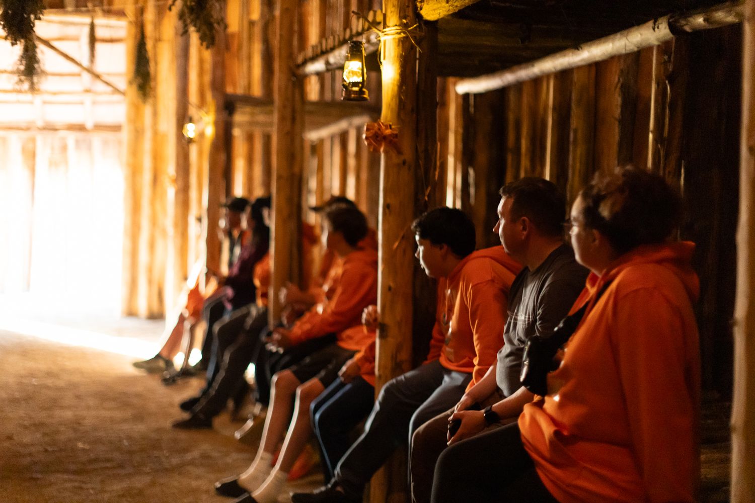 People seated along the walls inside dimly lit historic wooden building.