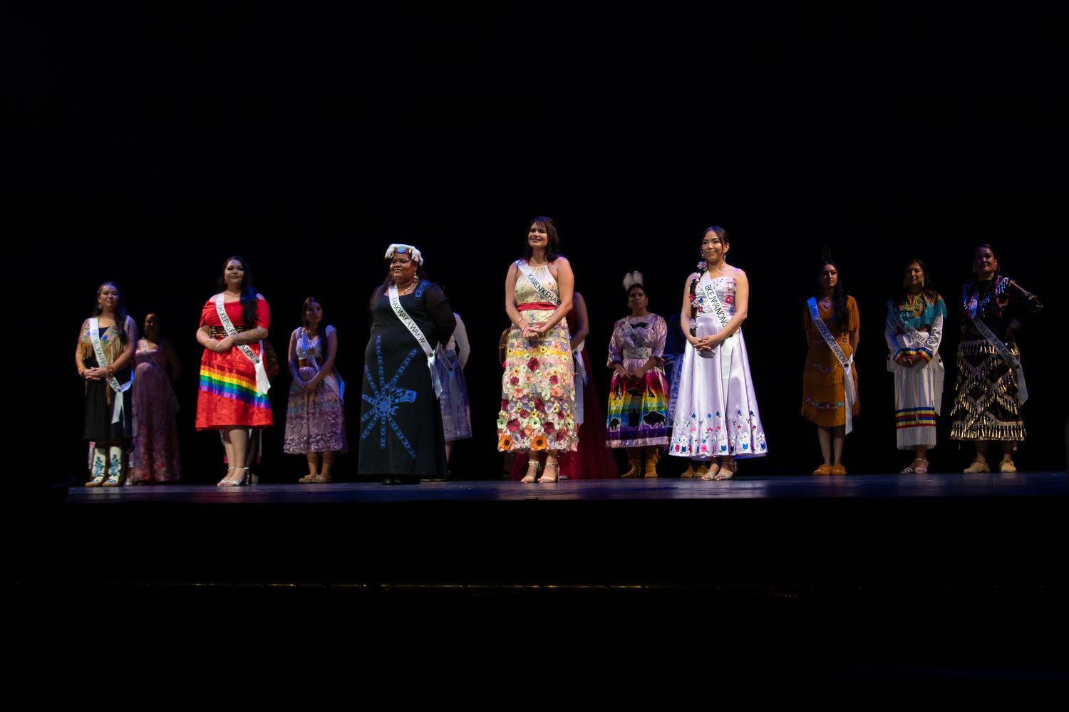Line of performers on dark stage wearing traditional dress.