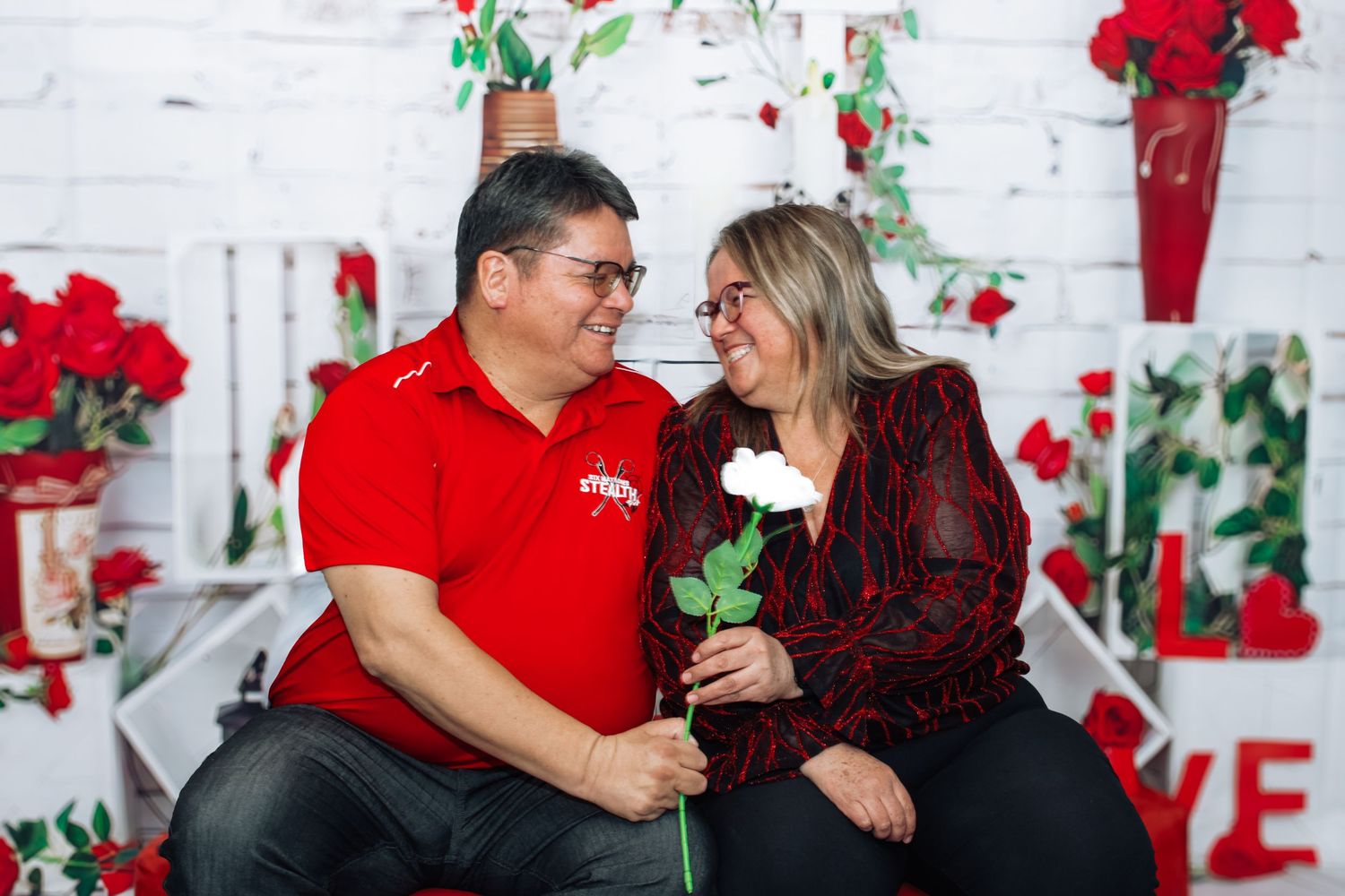 Romantic couple photo series with red roses and heart decorations on white brick background.