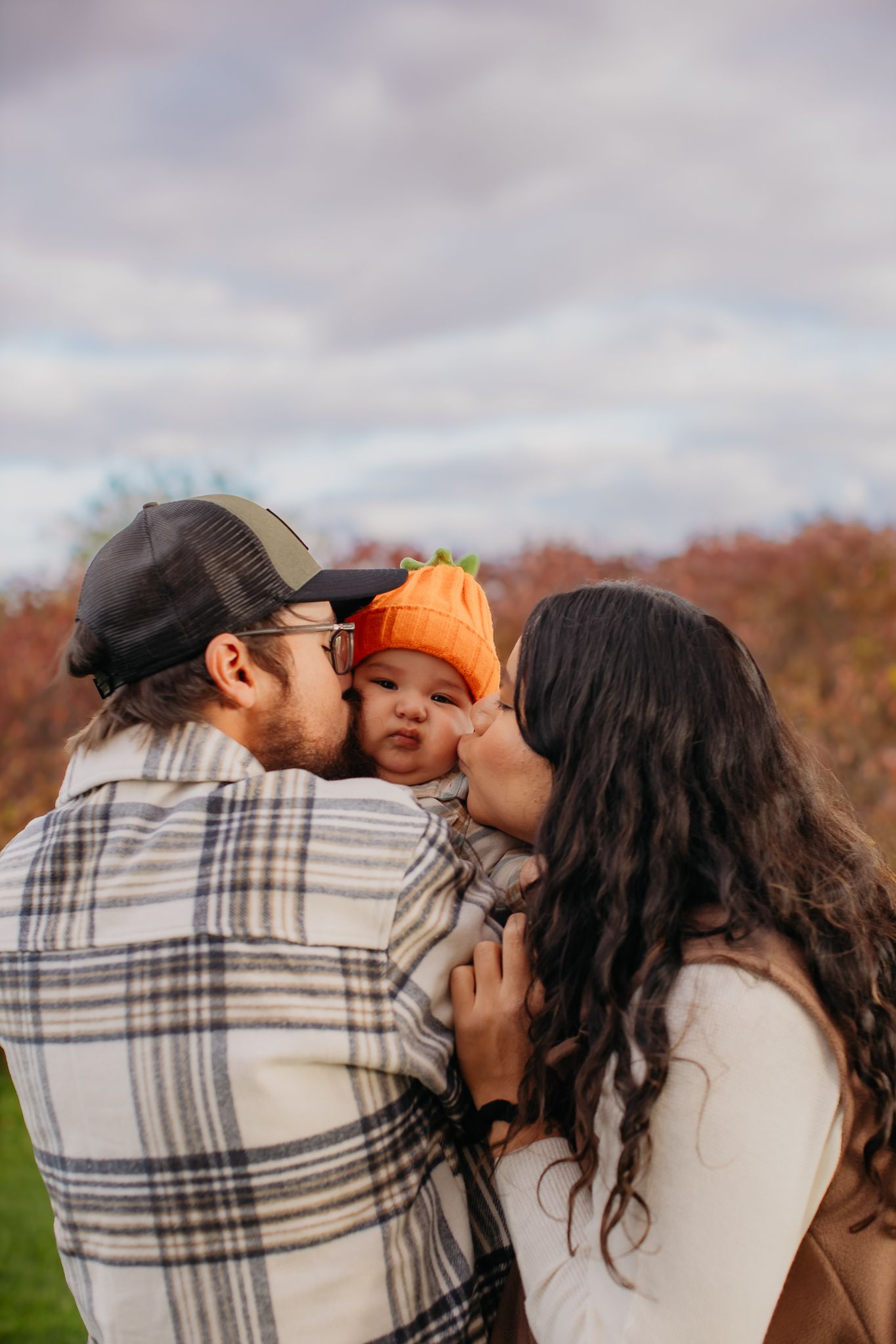 A family embraces outdoors against a backdrop of autumn trees and cloudy skies.