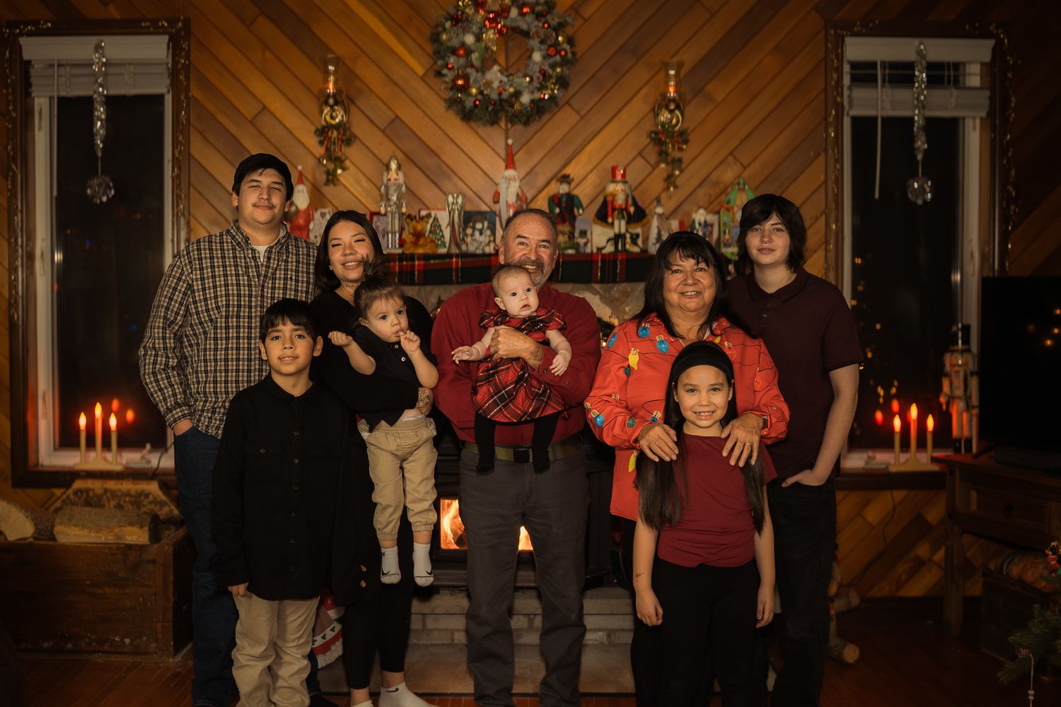 Group photo in front of a festive holiday backdrop with diagonal wood paneling and wreath.