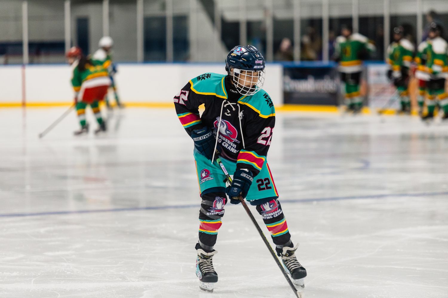 Youth ice hockey player in teal jersey number 22 skating on indoor rink during a game.