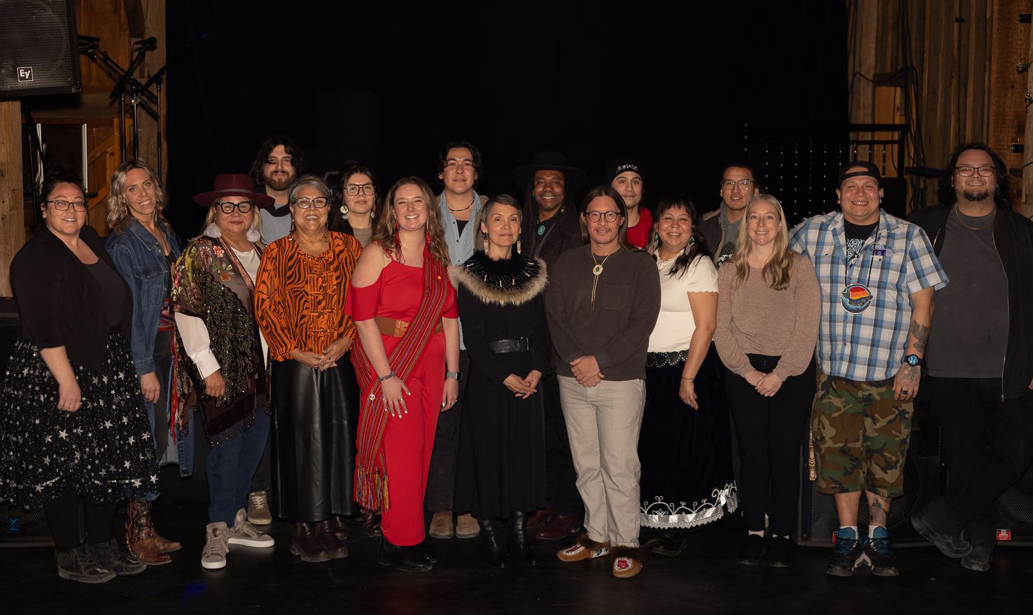 A large group of diverse performers pose together for a group photo on a theater stage after a show.